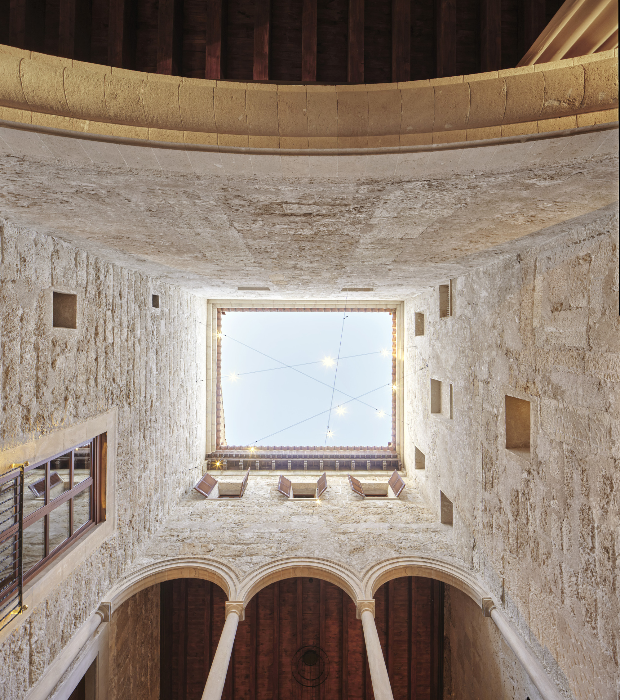 Upward view of the courtyard walls and a square opening to the sky, with strung lights above an arcade