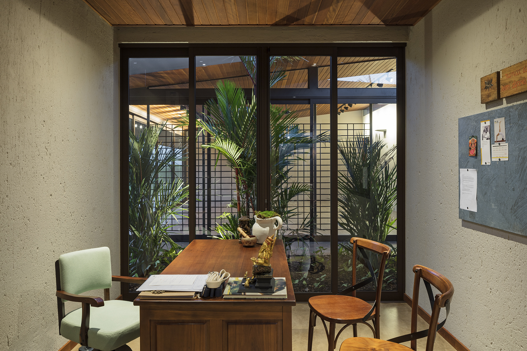 Small office with a wooden desk and bentwood chairs, facing a gridded glass wall onto a planted courtyard