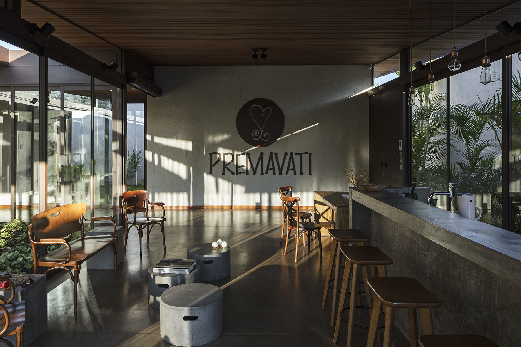 Café interior with a concrete counter, wooden stools and bentwood chairs, sunlight streaking across a wall bearing a heart logo and lettering