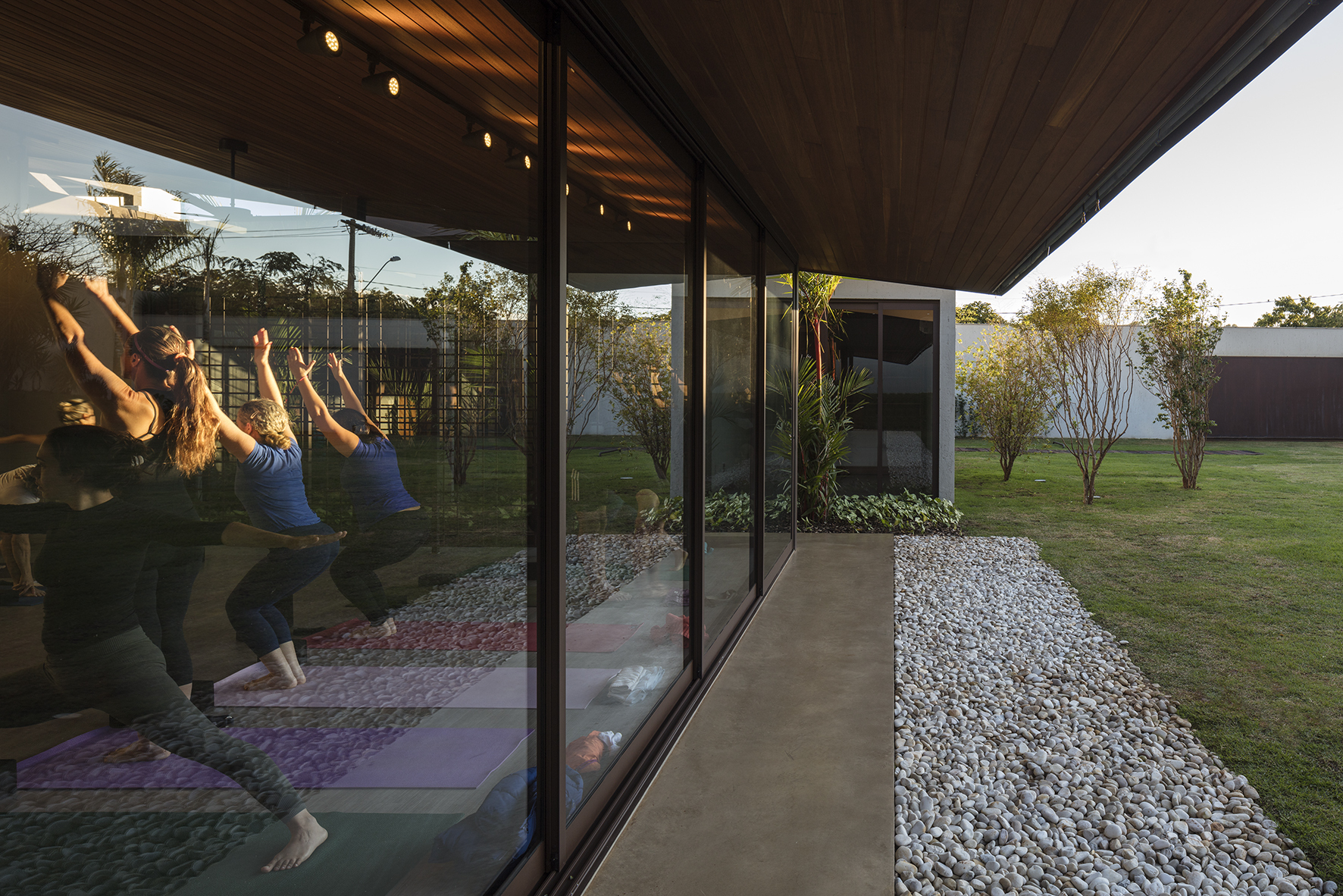 Yoga class reflected in the sliding glass wall at golden hour, with a pebble border and lawn beside the walkway