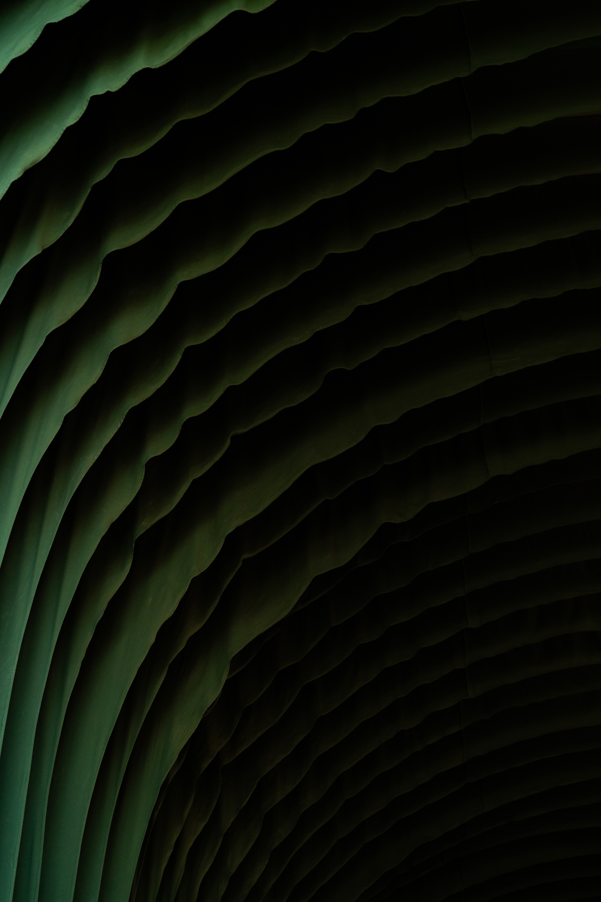 Detail of rippled dark green fabric folds curving across the ceiling in low, shadowed light
