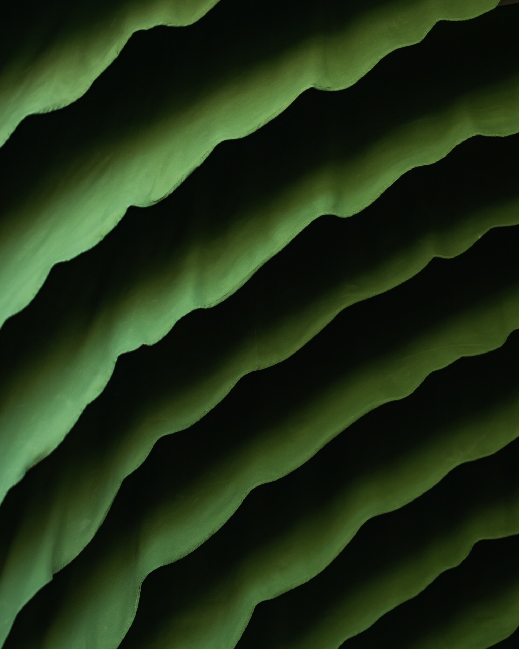 Close-up of rippled green wall surface with diagonal folds casting deep shadow in dim light