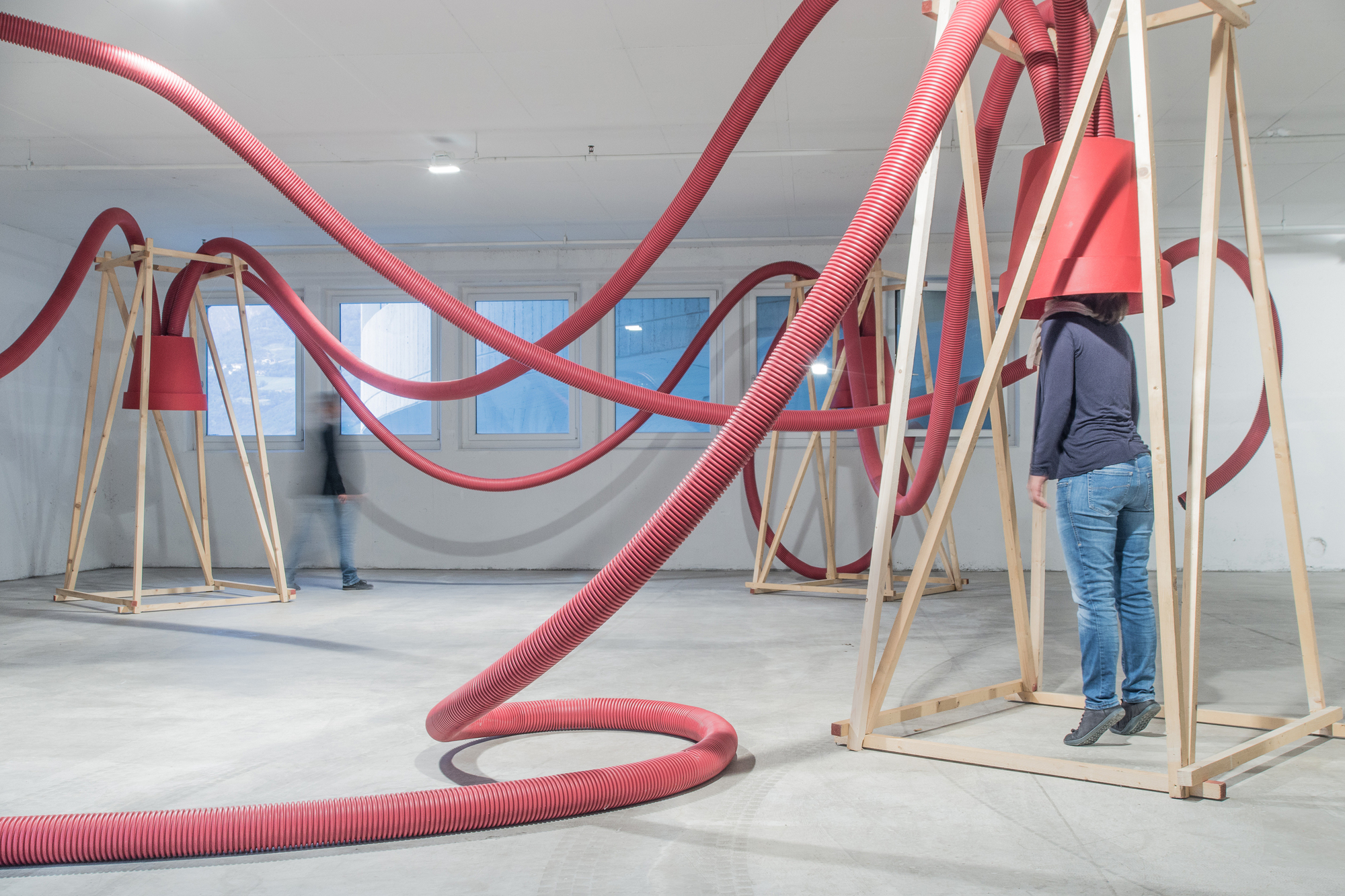 Red hose coiling on the concrete floor beside a timber frame, with a blurred figure walking past the windows