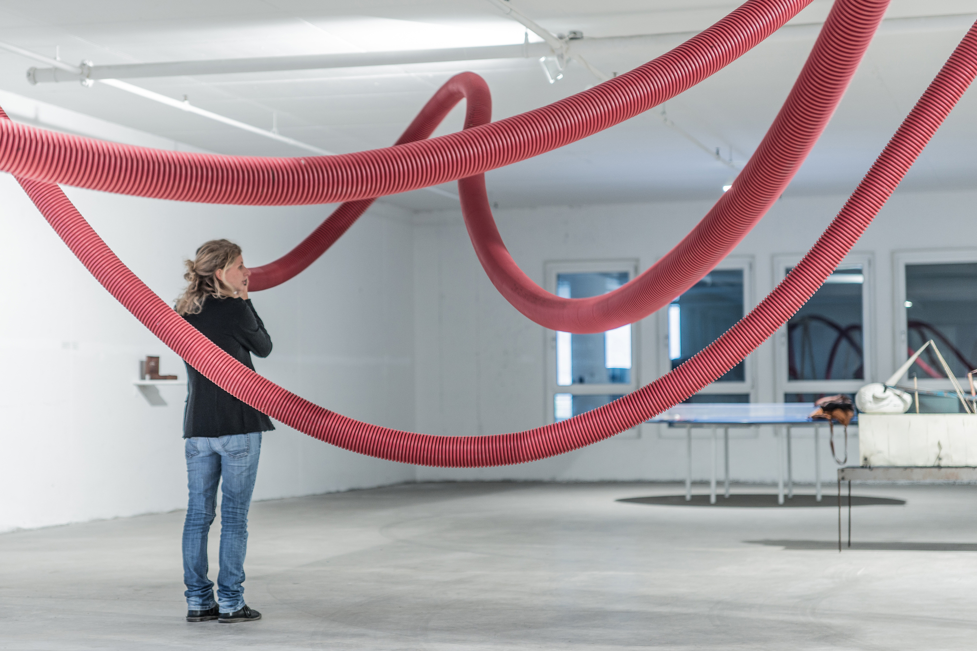 Visitor in a black jacket looking up at red hoses arcing overhead, with a ping-pong table behind