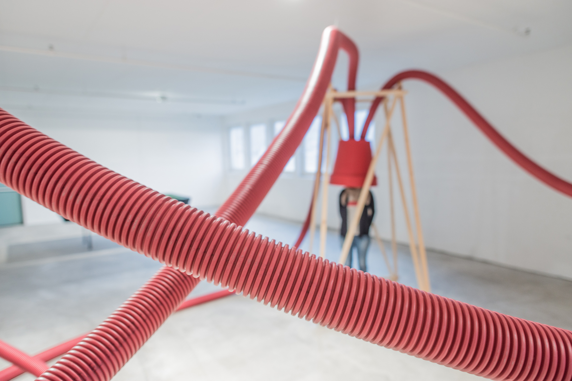 Close view of crossing red corrugated hoses in the foreground, with a blurred person under a bucket inside a wooden frame behind
