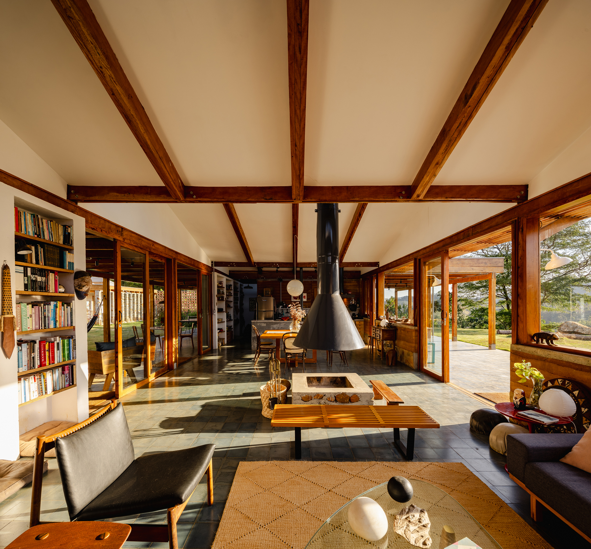 Long living room with exposed timber beams, a central hanging fireplace, built-in bookshelves and slate floor in raking light