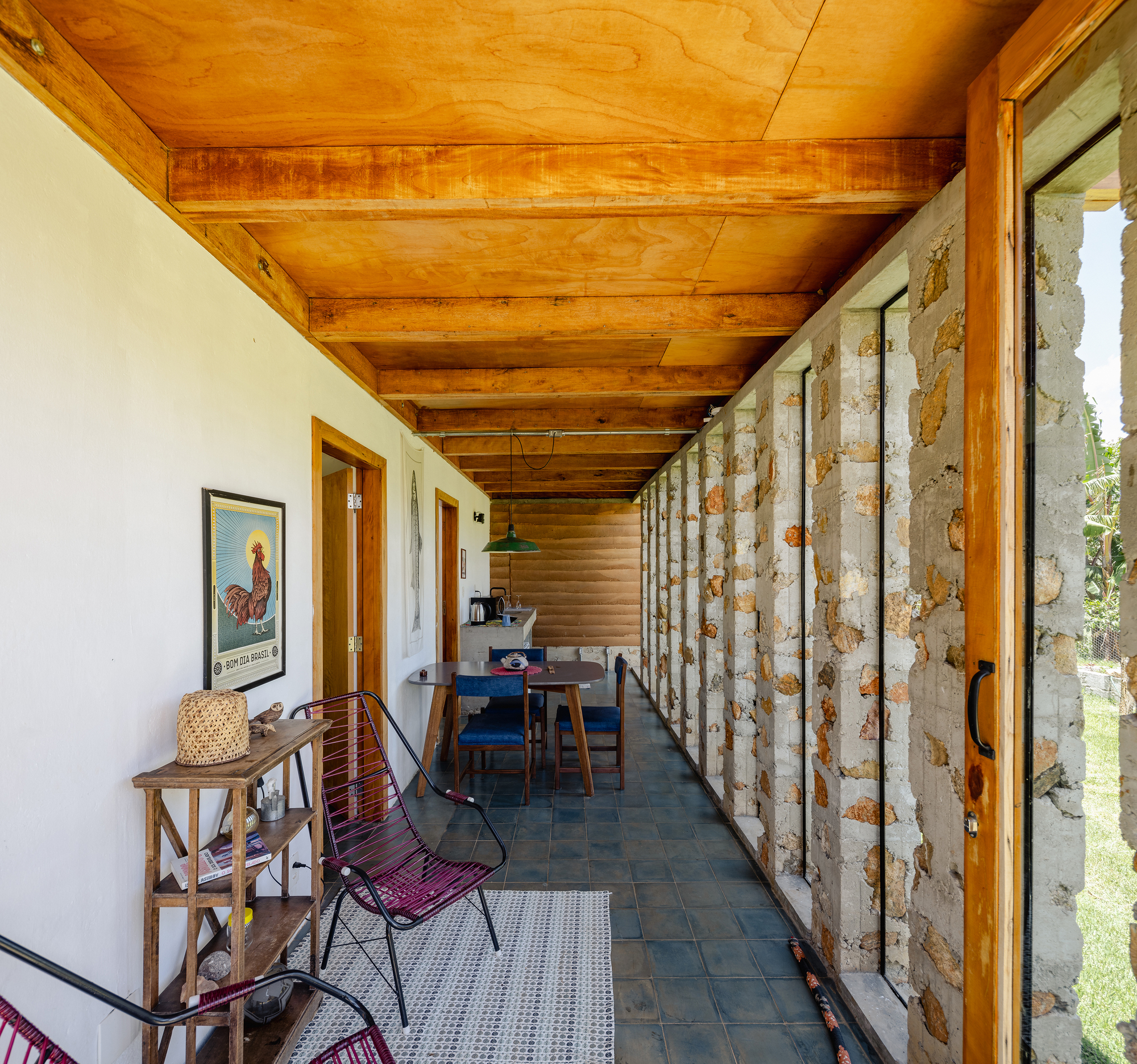 Covered gallery with rubble stone wall on one side, slate floor, timber ceiling and a dining table, in bright daylight