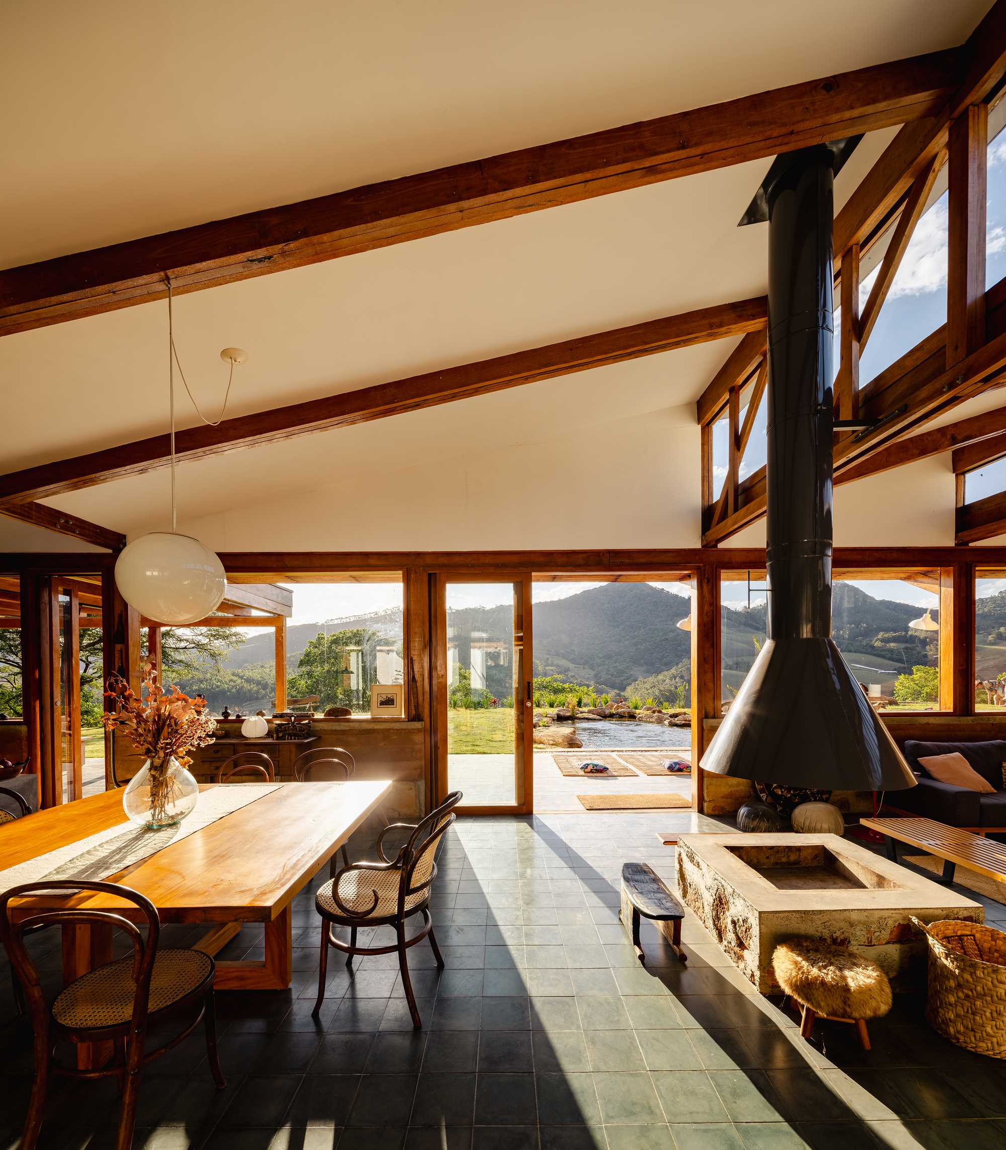 Open living and dining room with a suspended black fireplace hood, exposed roof beams and mountain views in low sun