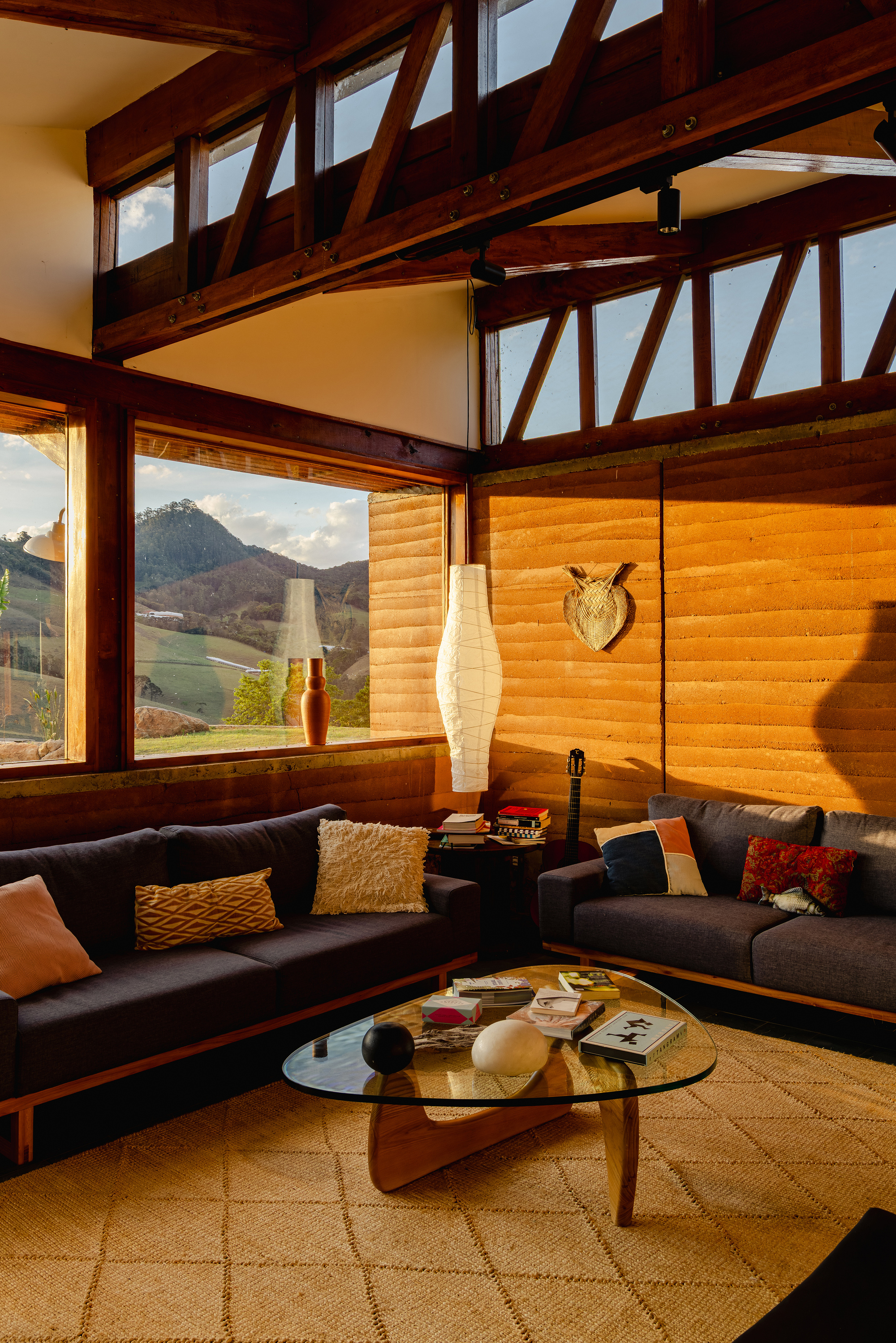 Seating corner with dark sofas, a glass-topped wood coffee table and a rammed earth wall glowing in late sunlight