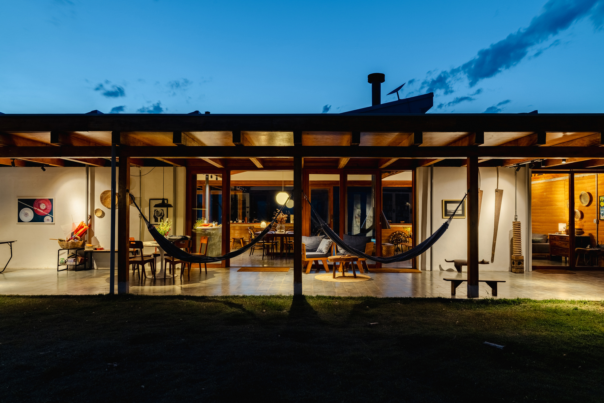Garden-side view of the open timber pavilion with two black hammocks strung between posts under a deep blue evening sky