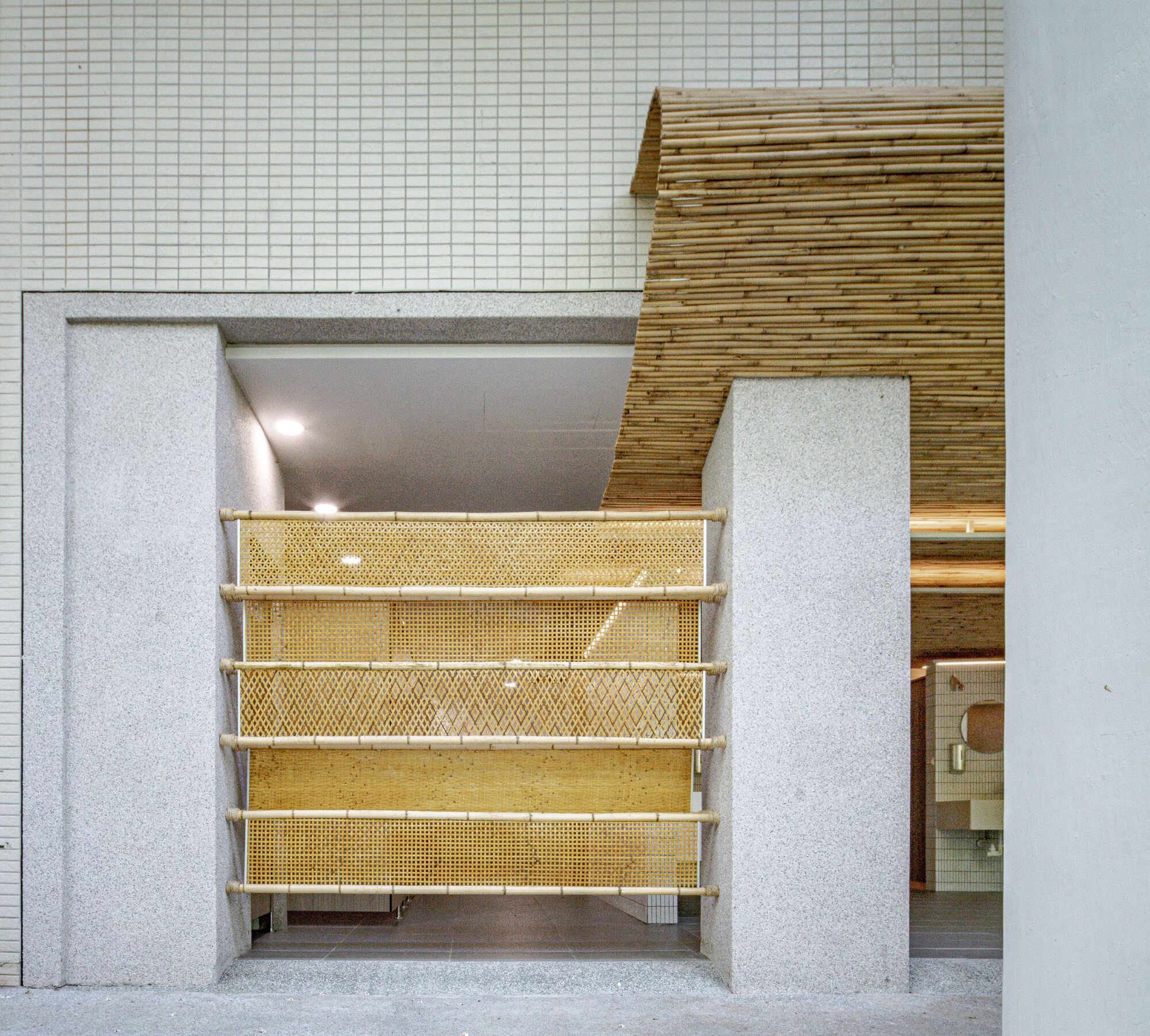 Entrance screened by woven rattan panels on bamboo rails between stone piers, with a curling bamboo roof edge above white tile