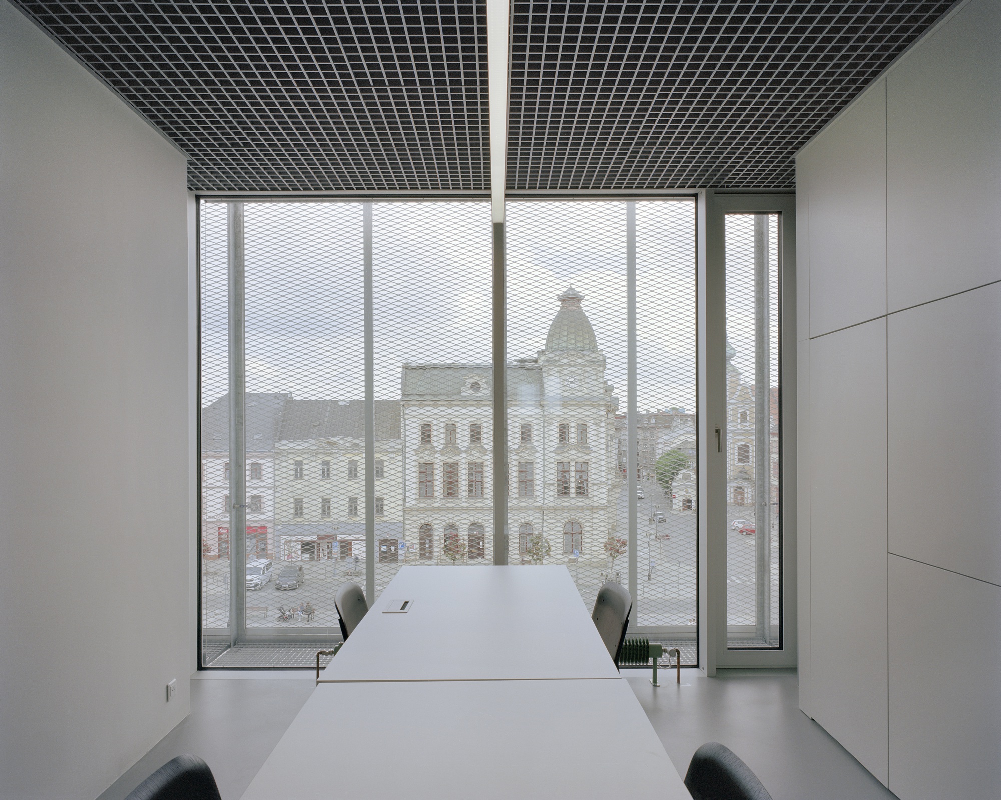 Meeting room with a long white table facing a floor-to-ceiling window, mesh screen and a domed historic building beyond
