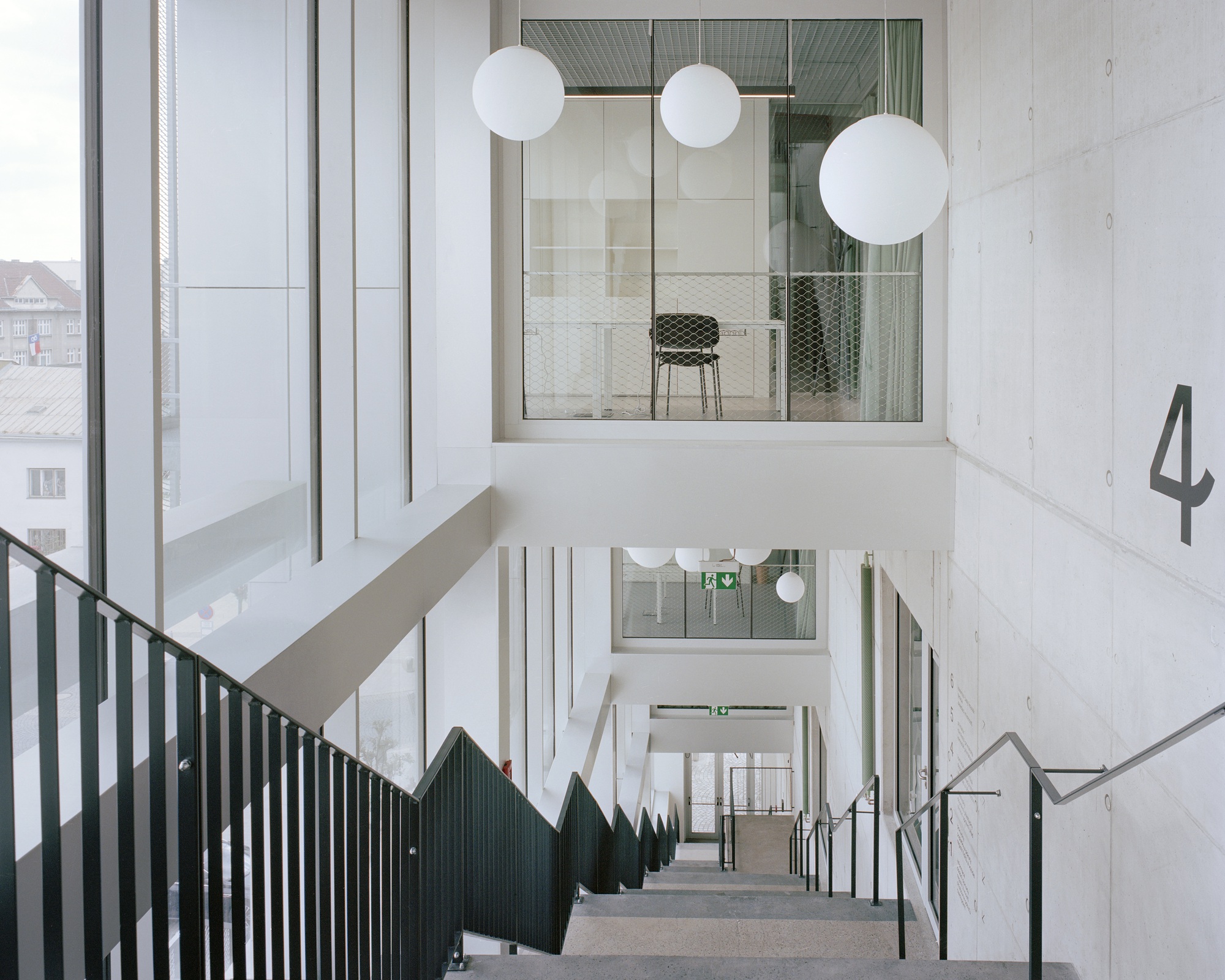 Concrete stairwell with dark steel balustrades and white globe pendants, a glazed meeting room visible above and the number 4 on the wall