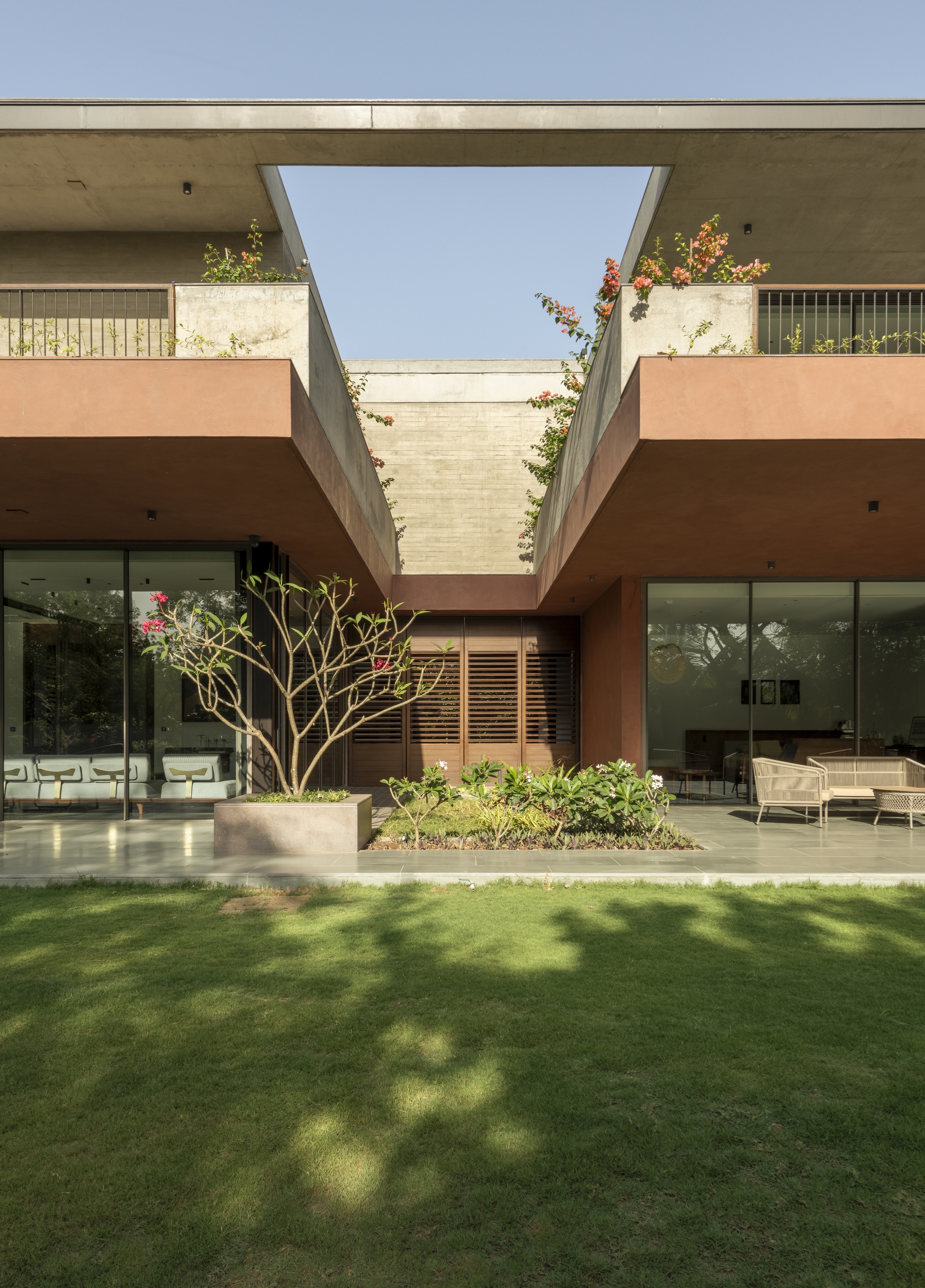 Garden elevation where terracotta balconies cantilever over glazed rooms, with a frangipani in a planter and bougainvillea spilling from the roof gap