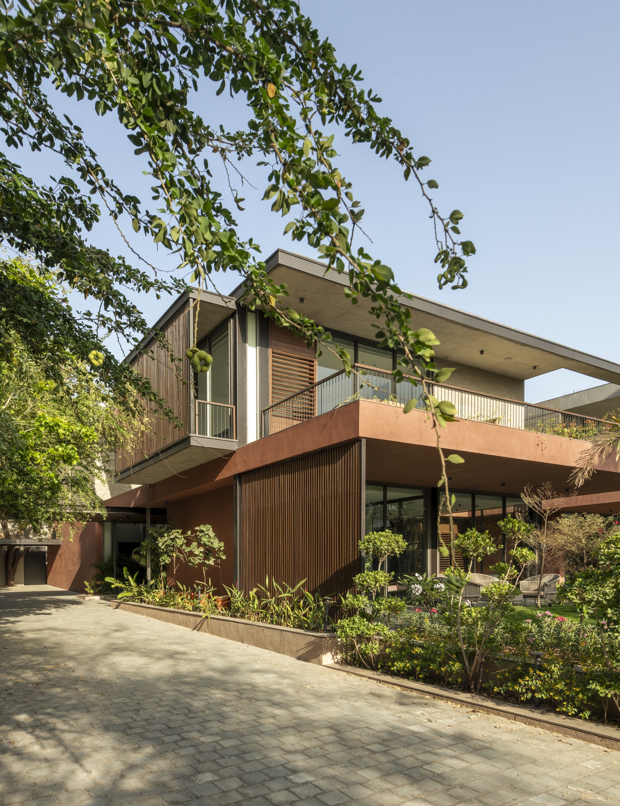 Entrance side of the house with timber slat screens, planted beds and a paver drive dappled by tree shade