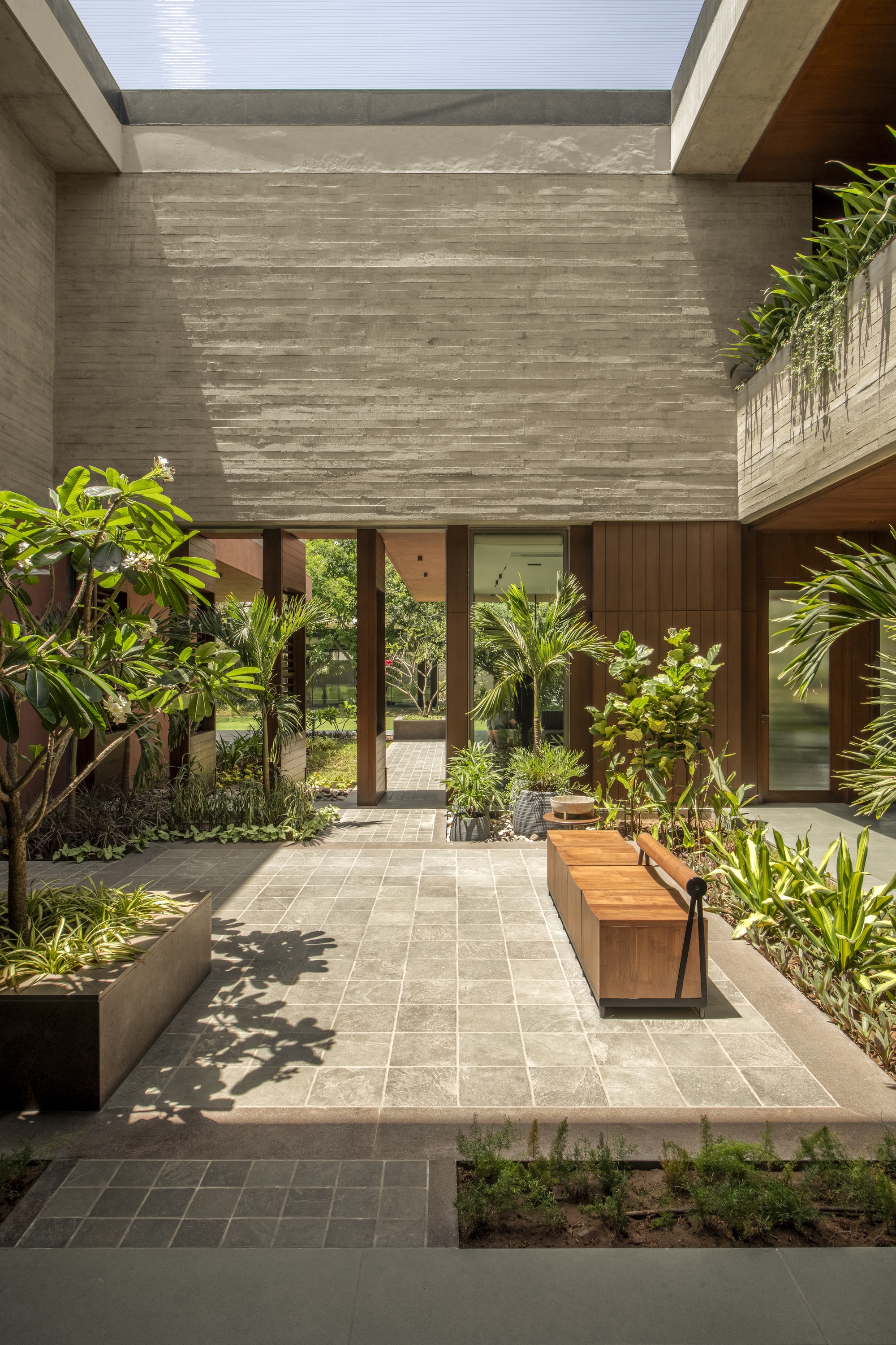 Courtyard with a timber bench on stone paving beneath a board-marked concrete wall, tree shadows falling across the floor in sunlight