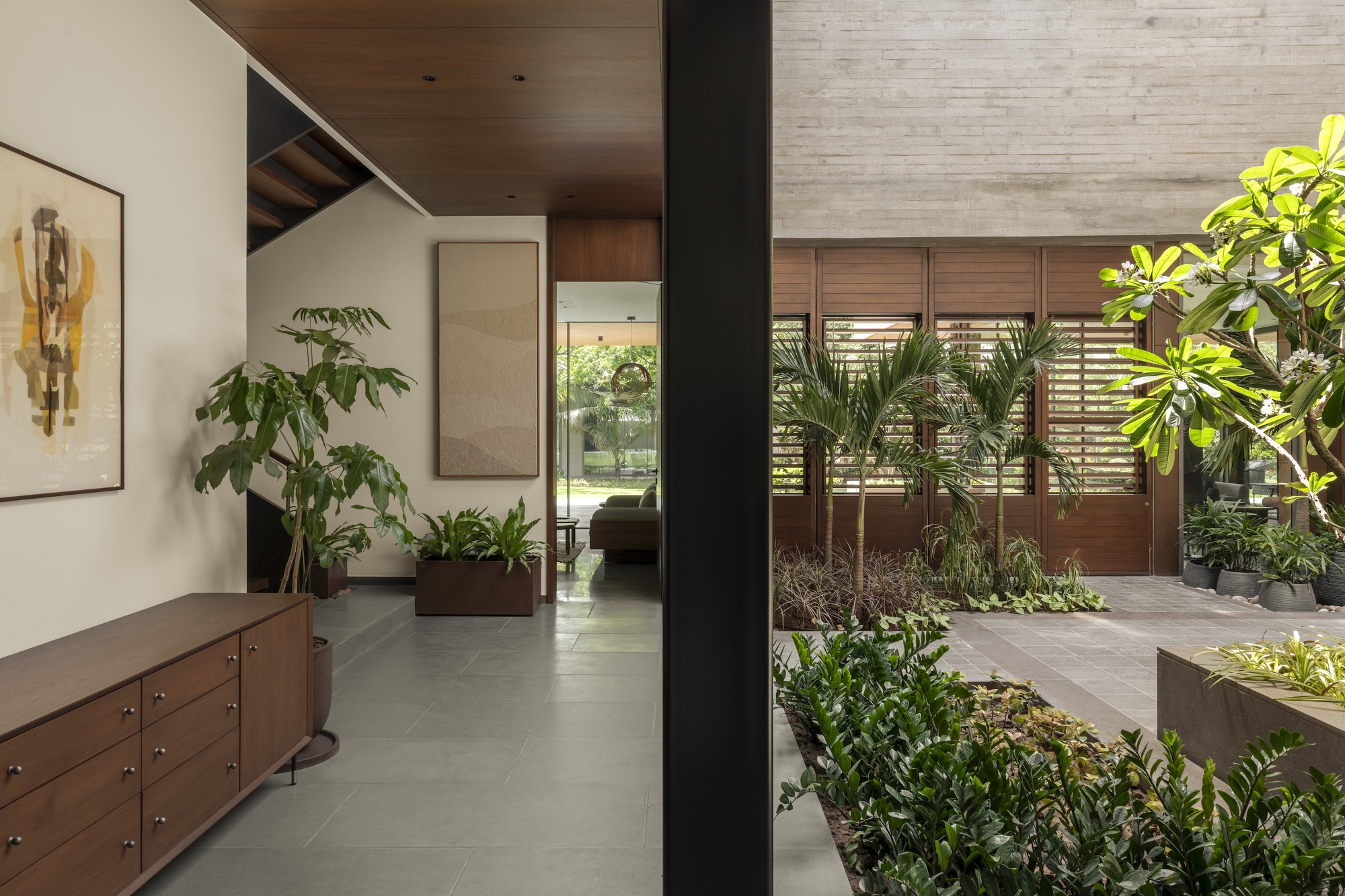Walnut sideboard and framed abstract painting beside a black column, looking across to louvred timber shutters and palms