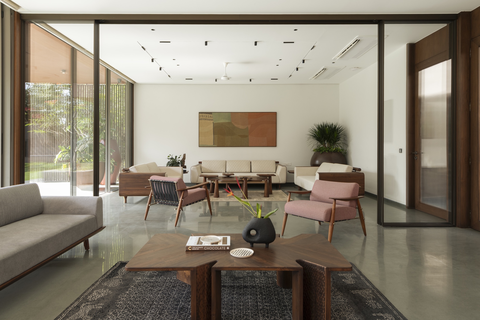 Living room with pink armchairs, a faceted walnut coffee table and a glazed sliding wall opening to a green garden