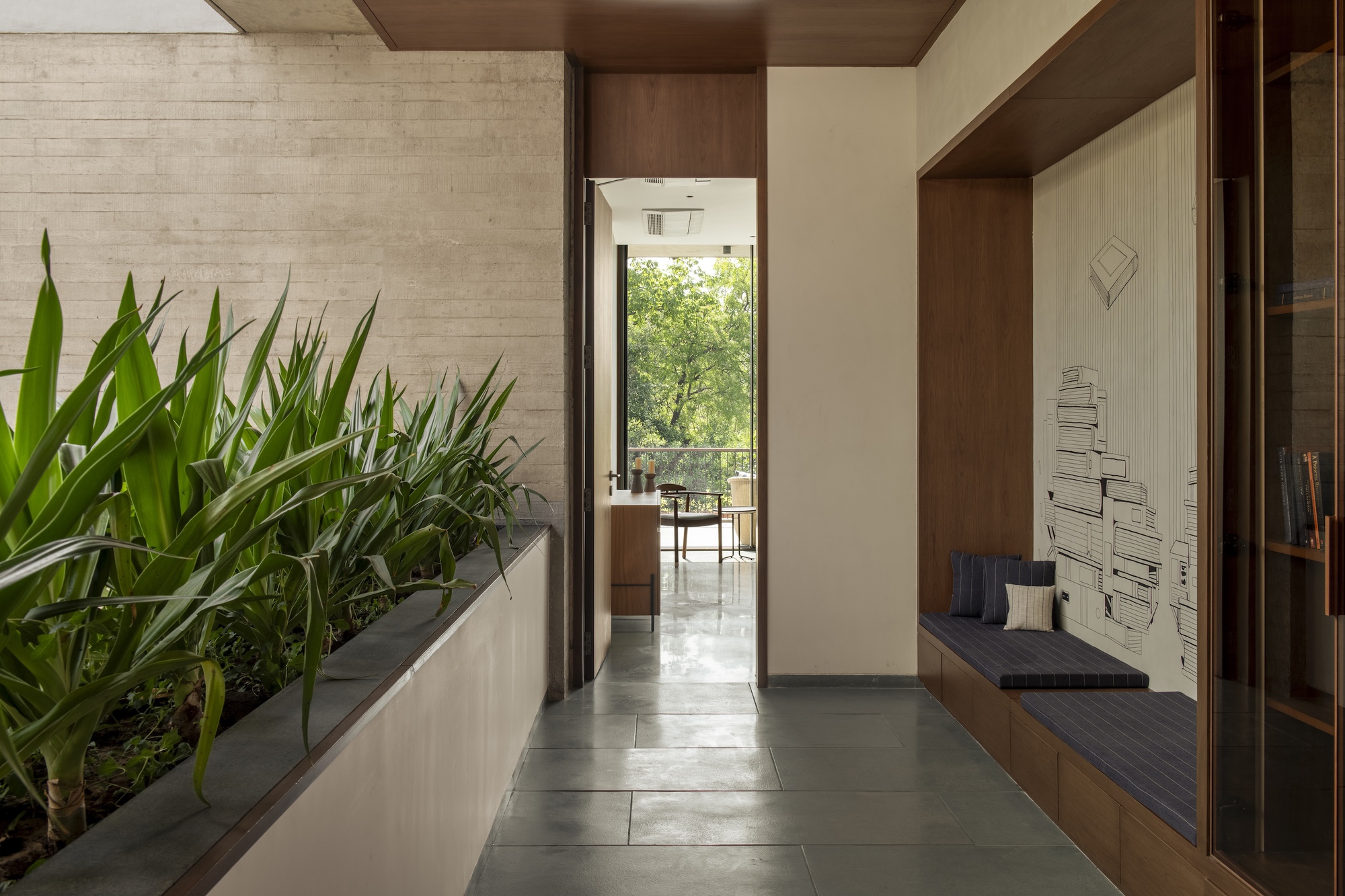 Corridor lined with a raised planter of agave-like leaves on one side and a built-in timber window seat with cushions on the other