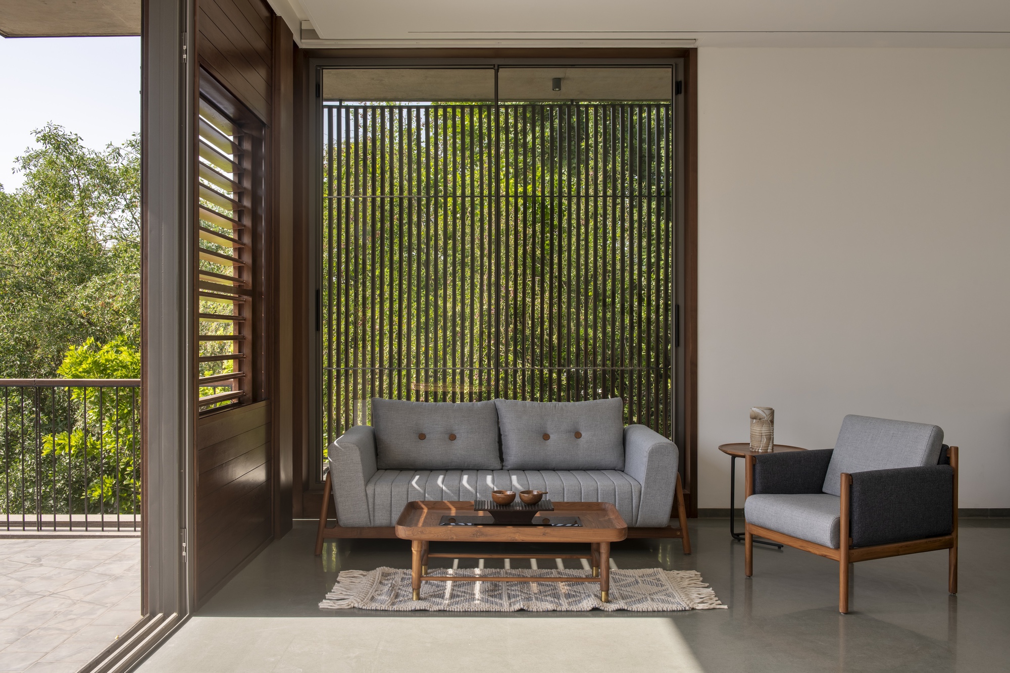 Living area with grey sofa and walnut coffee table facing a vertical timber slat screen and green foliage in daylight
