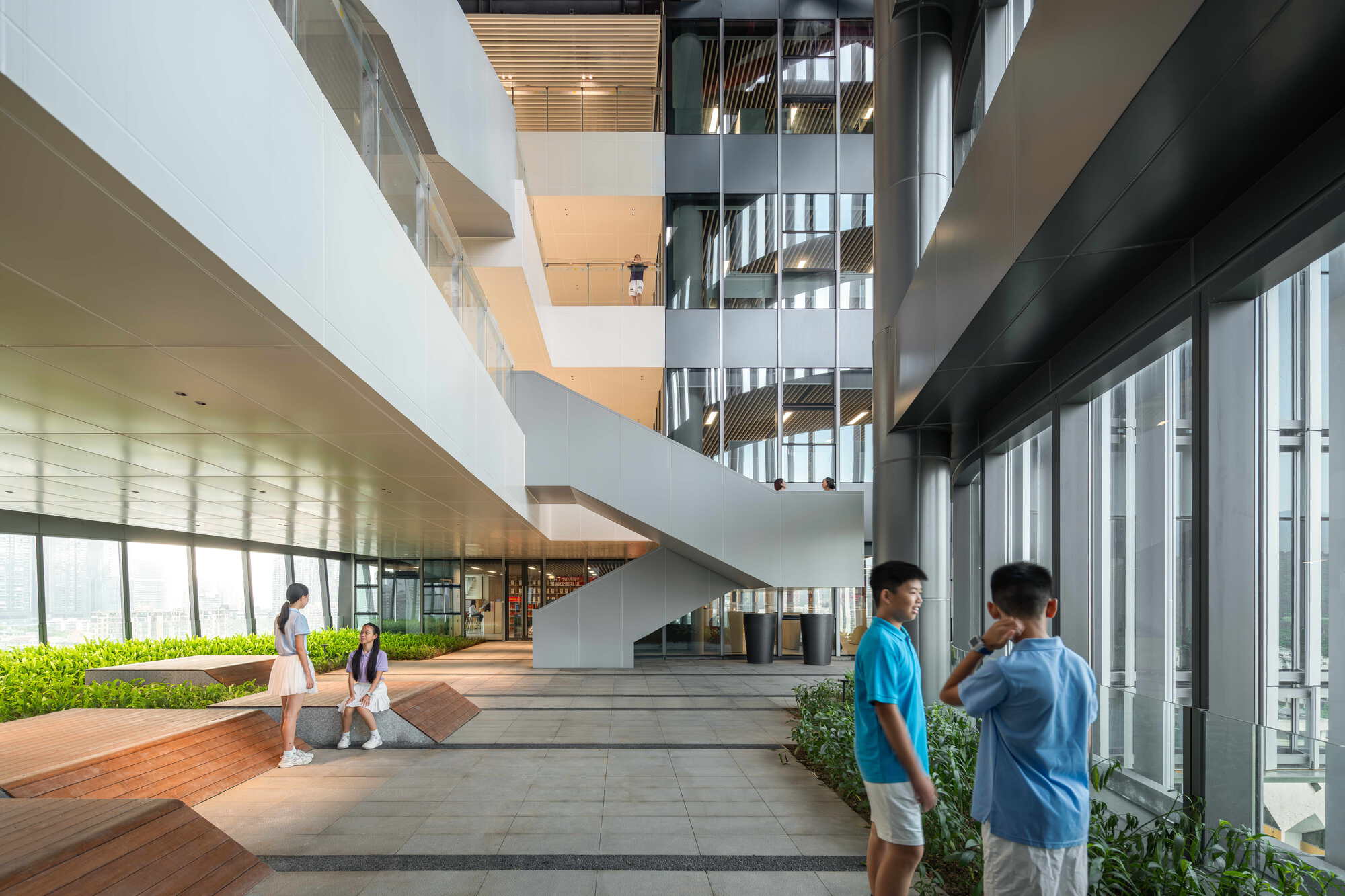 Open terrace with a white stair, timber benches and planted beds, with students standing in daylight