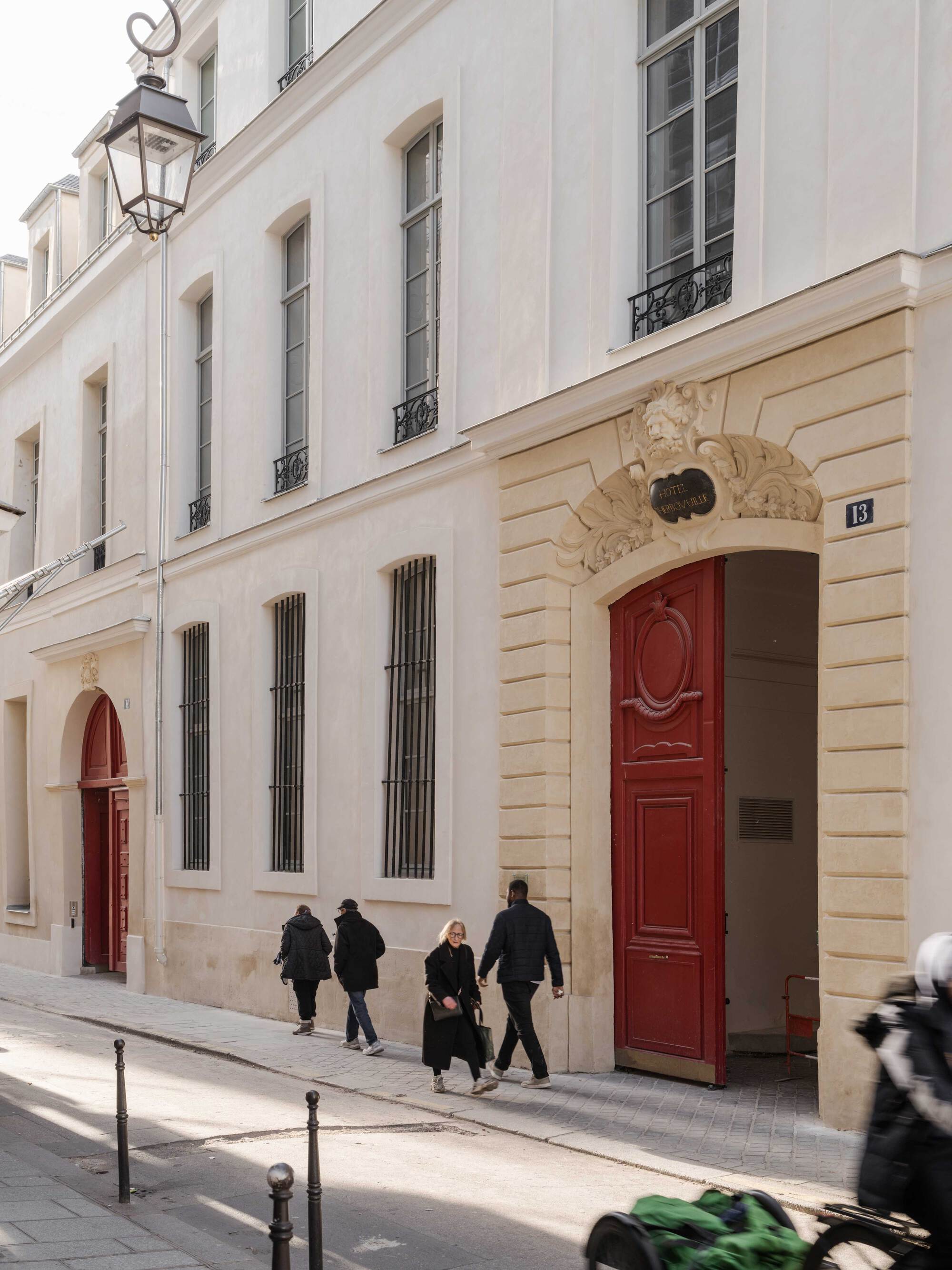 Stone-framed arched carriage entrance with a tall red timber door and pedestrians passing along a paved street in daylight
