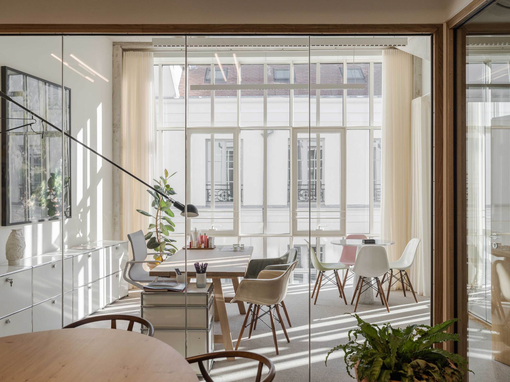 Glazed meeting room with a long table, molded chairs and potted plants, sun casting stripes across the carpet