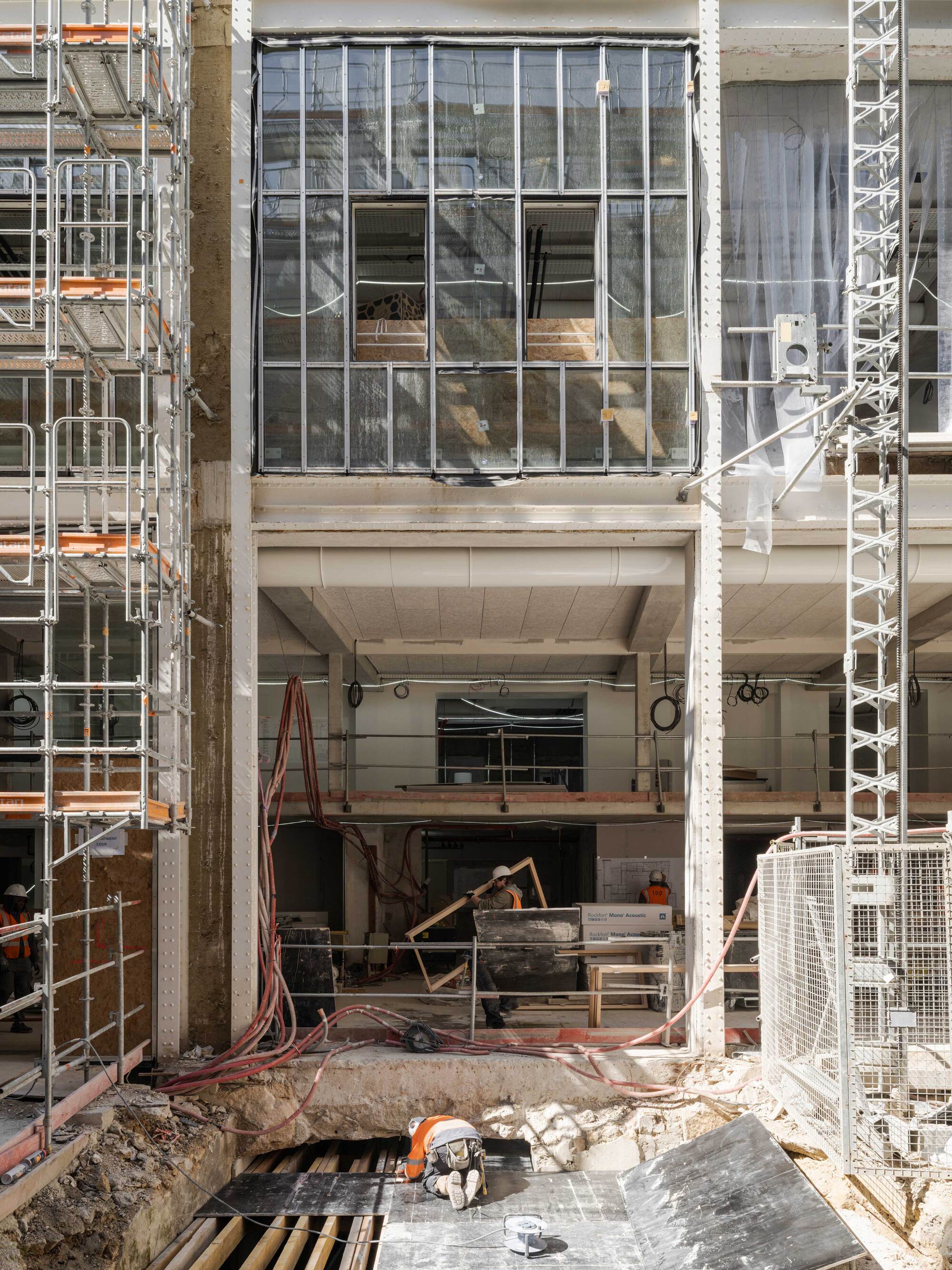 Close view of a gridded steel-framed glass bay above an open concrete floor, with a worker kneeling near cables below