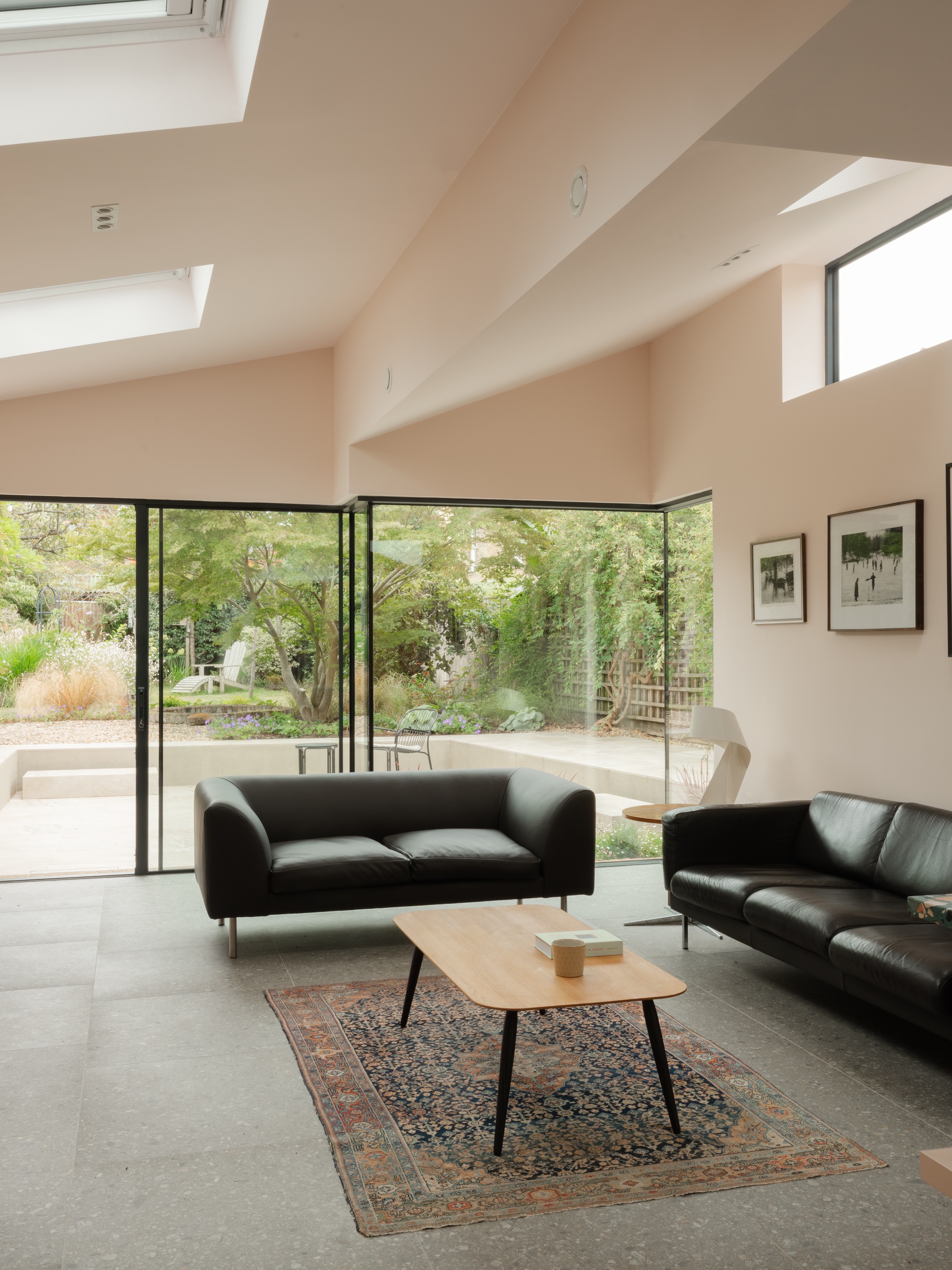 Living area with black leather sofas, a patterned rug and corner glazing framing a garden tree, with rooflights overhead