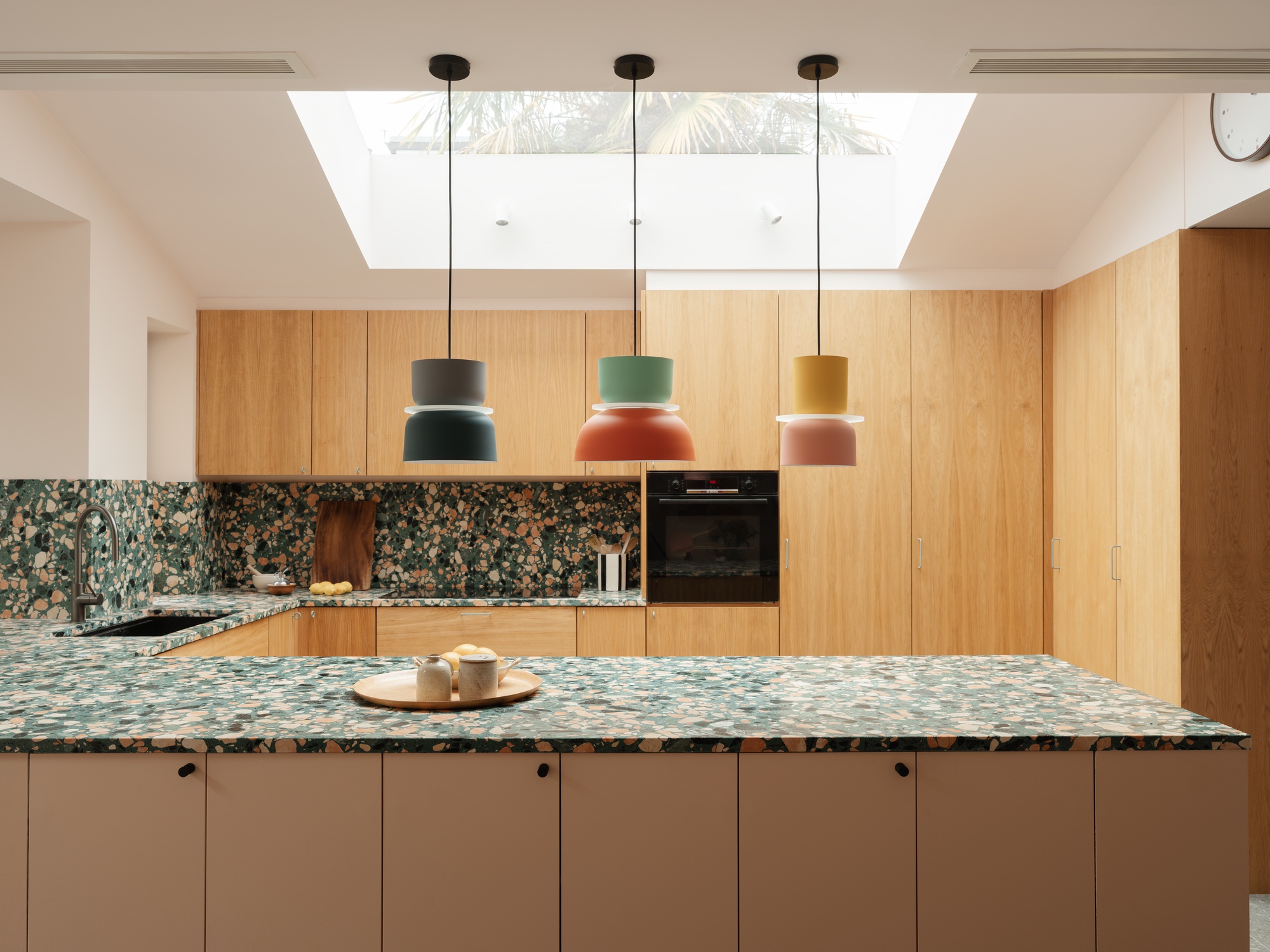 Frontal view of the terrazzo-topped island and oak cabinets, with three pendant lights hanging below a daylit rooflight