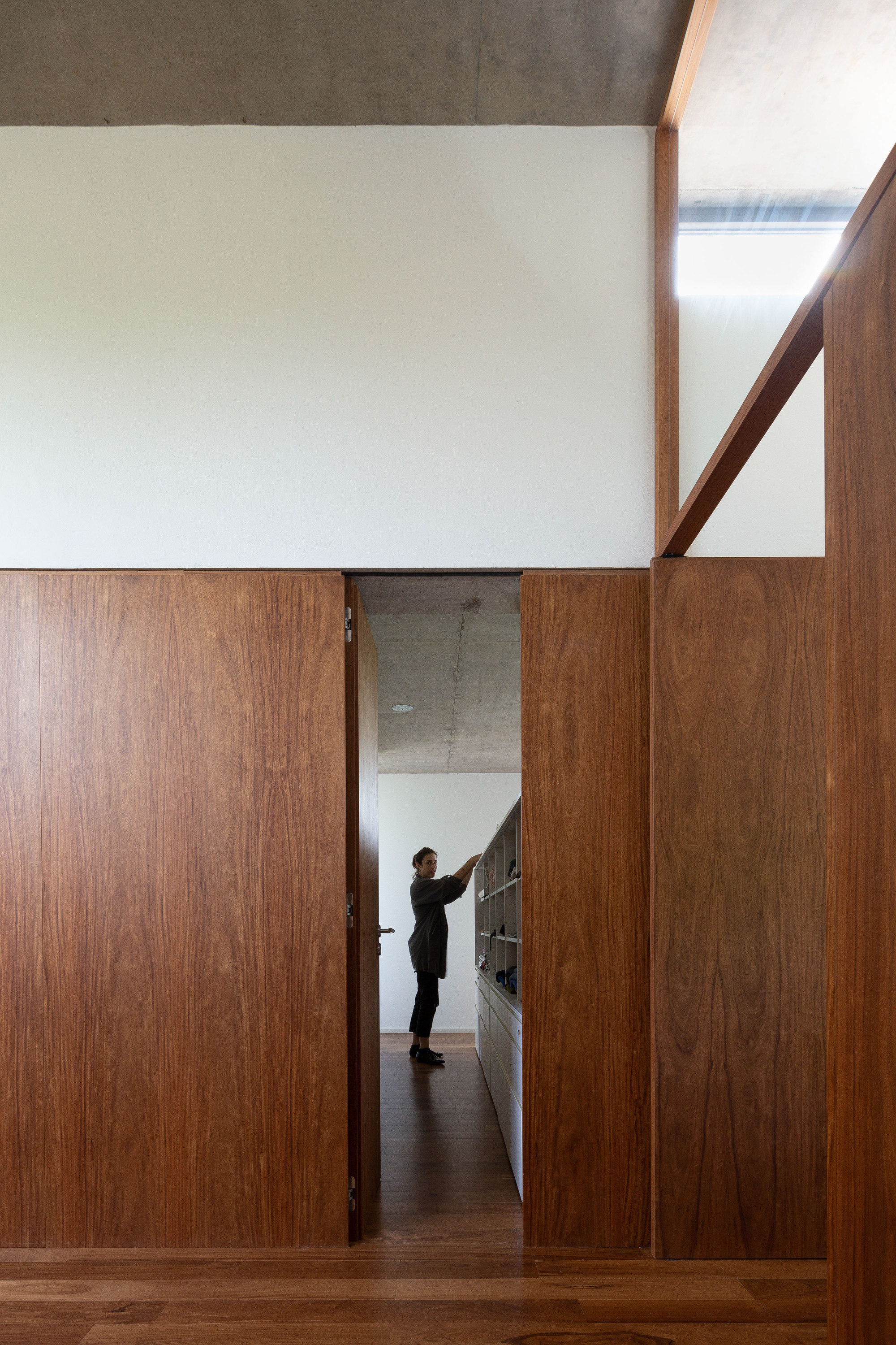 Wood-paneled doorway opening onto a corridor where a person reaches toward a shelf, with a skylight slot above