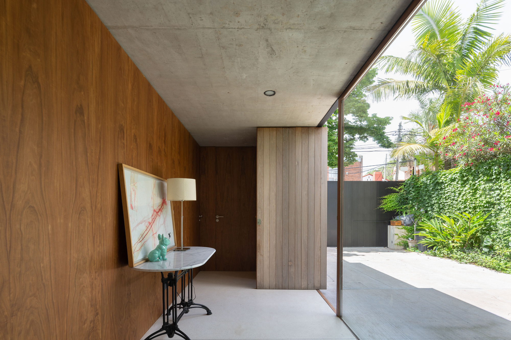 Entry hall with walnut wall panels, a marble console table and a glass wall facing a palm tree and ivy hedge