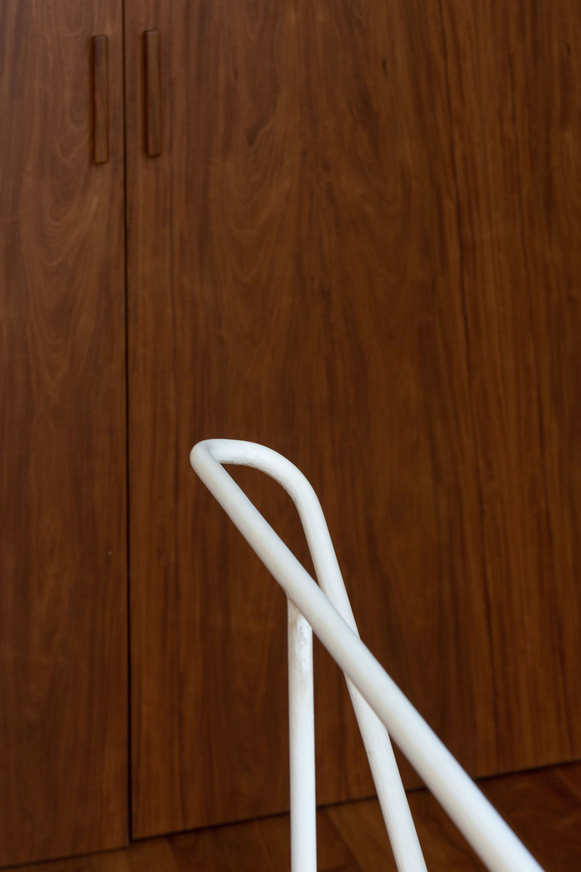 Close-up of a white tubular steel chair back in front of walnut cabinet doors with recessed wooden pulls