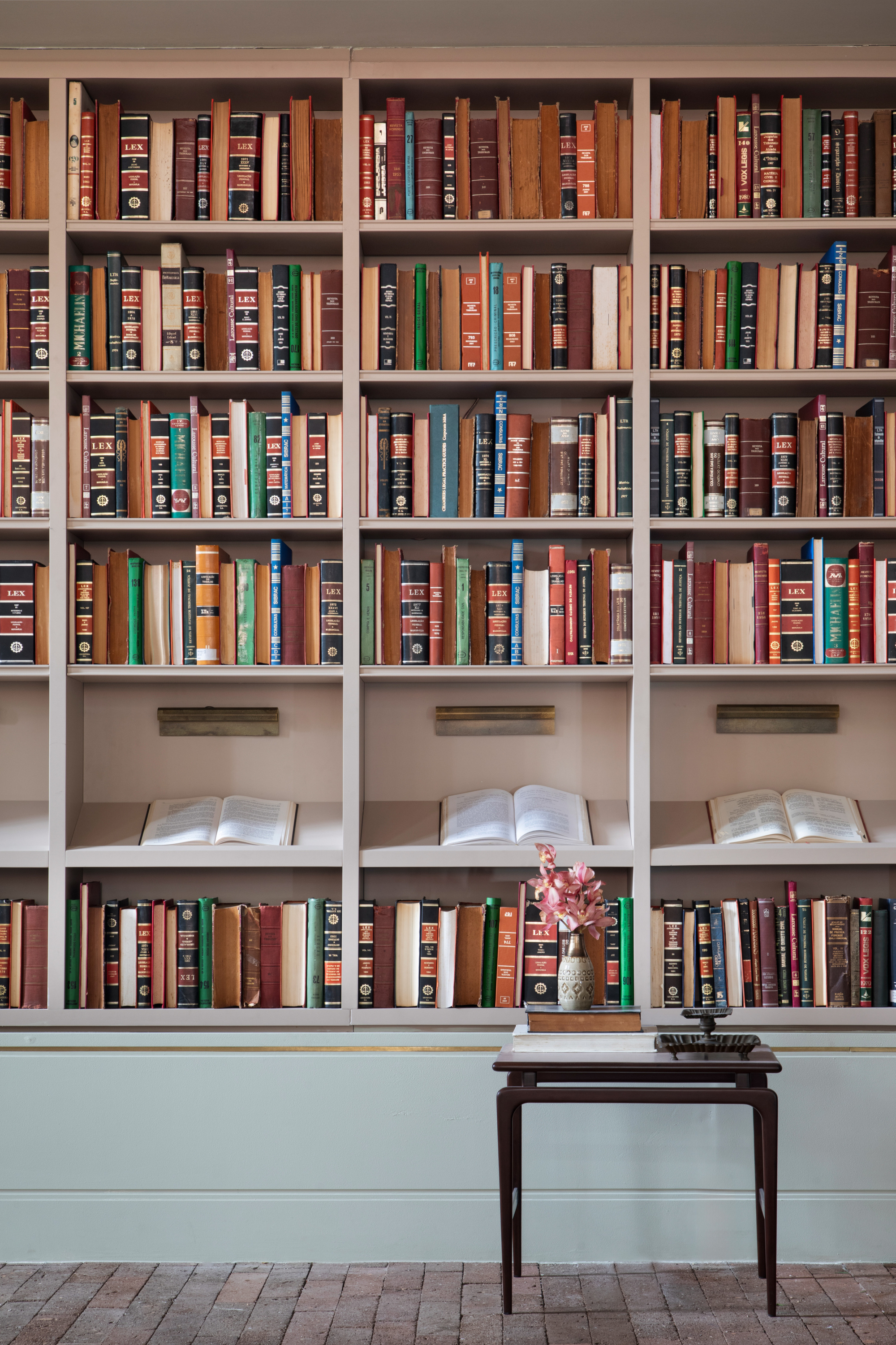 Built-in bookshelf wall of leather-bound volumes with open books on display ledges above a small dark wood table with pink blooms