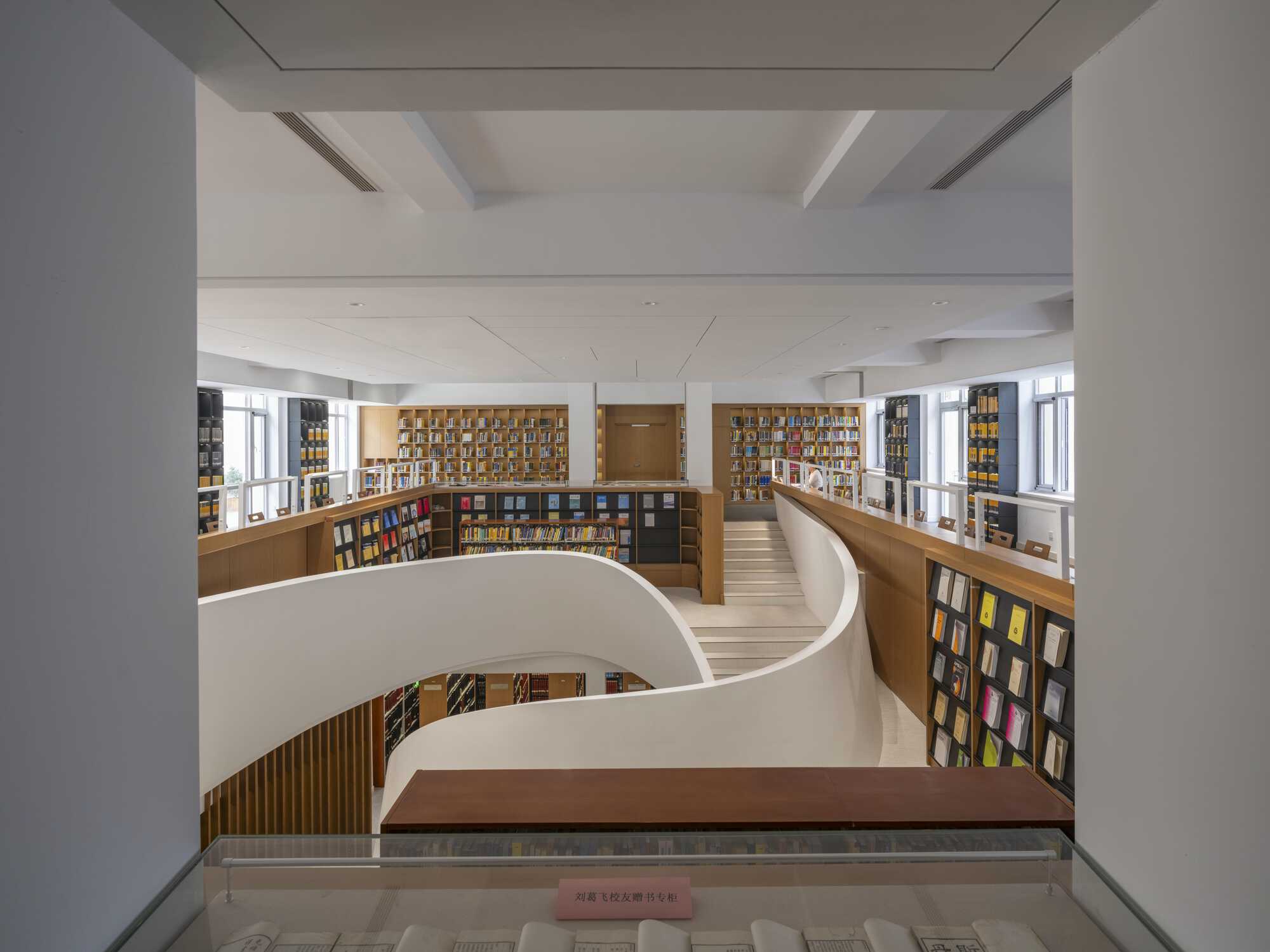 View through a white opening onto the curved stair walls and wood-clad bookshelves of a multi-level library reading hall