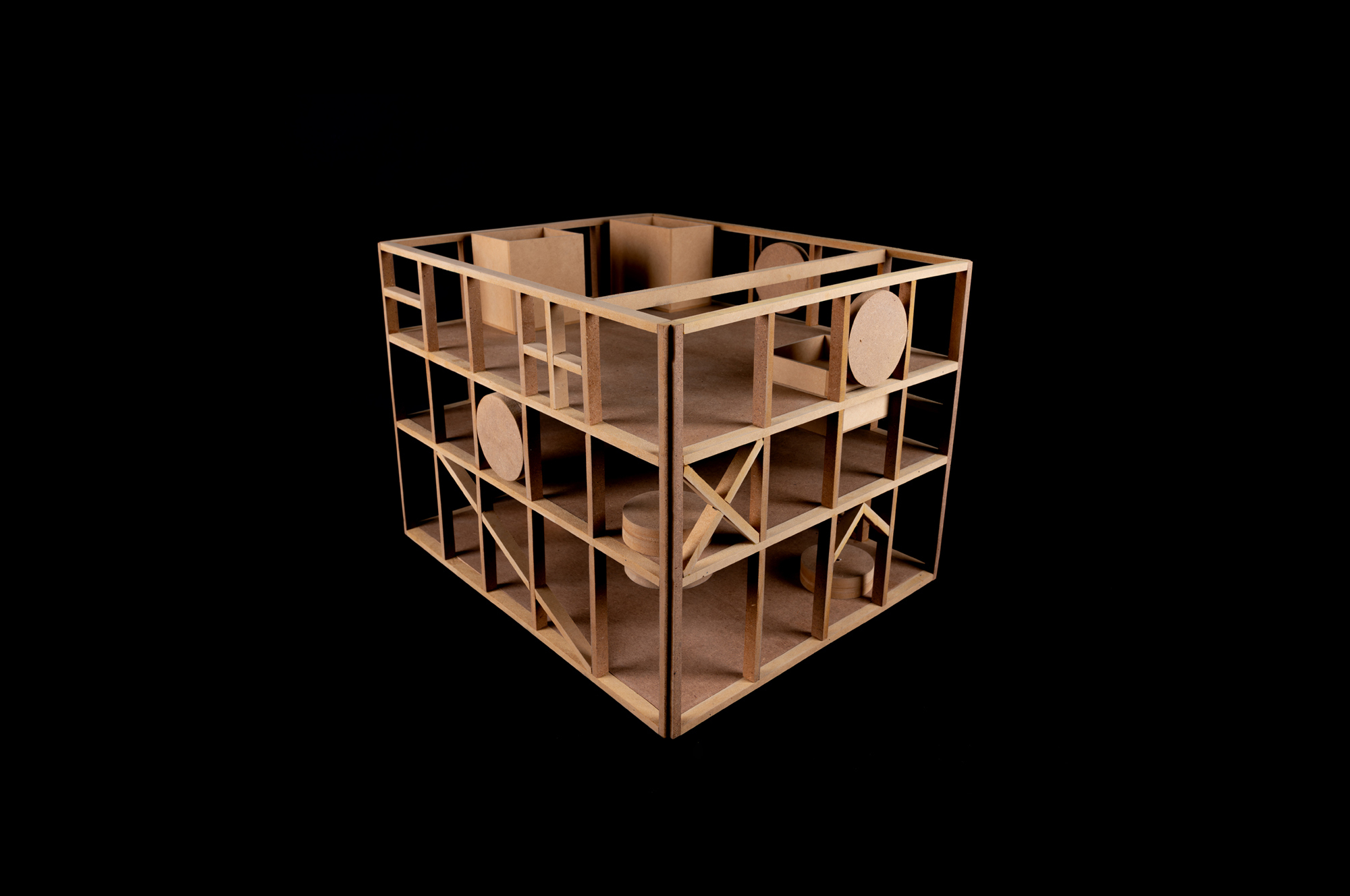 Physical model of a timber-framed cube with diagonal bracing, stacked floor plates and circular discs, lit against a black background