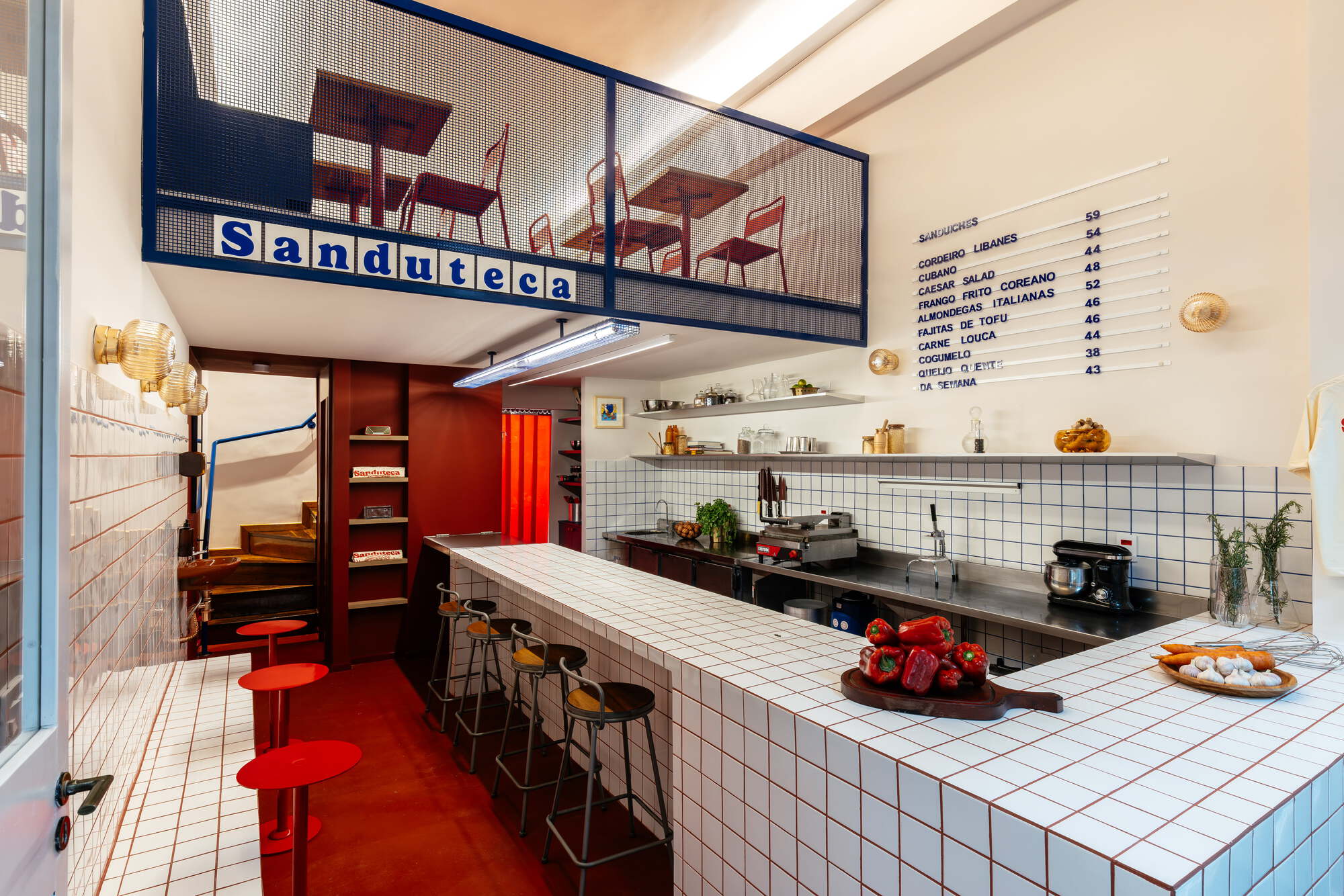 Angled view of the tiled counter with a board of red peppers, round red stools and the mezzanine sign above