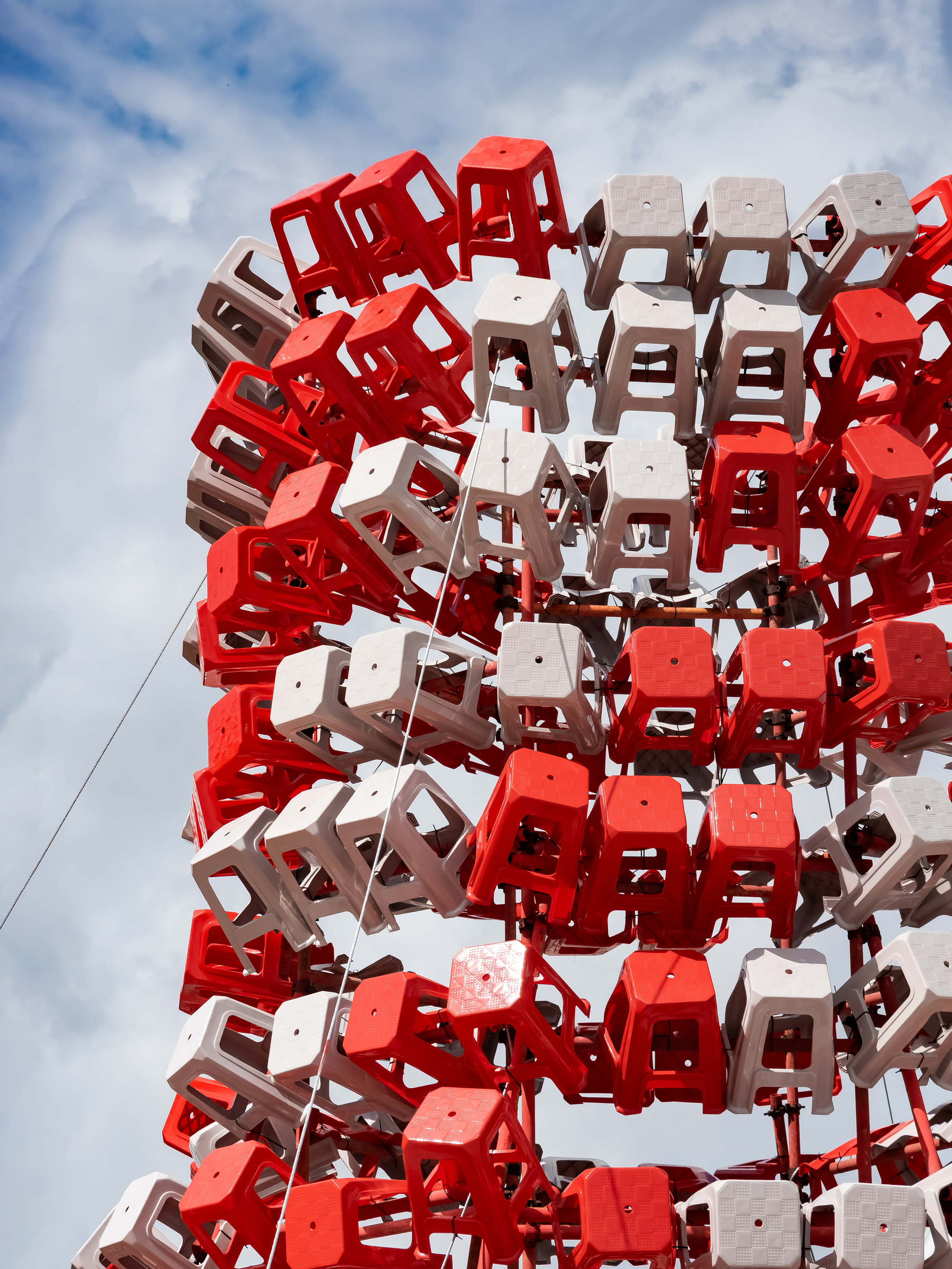 Close-up of red and white plastic stools mounted on a steel frame against a blue sky with thin clouds