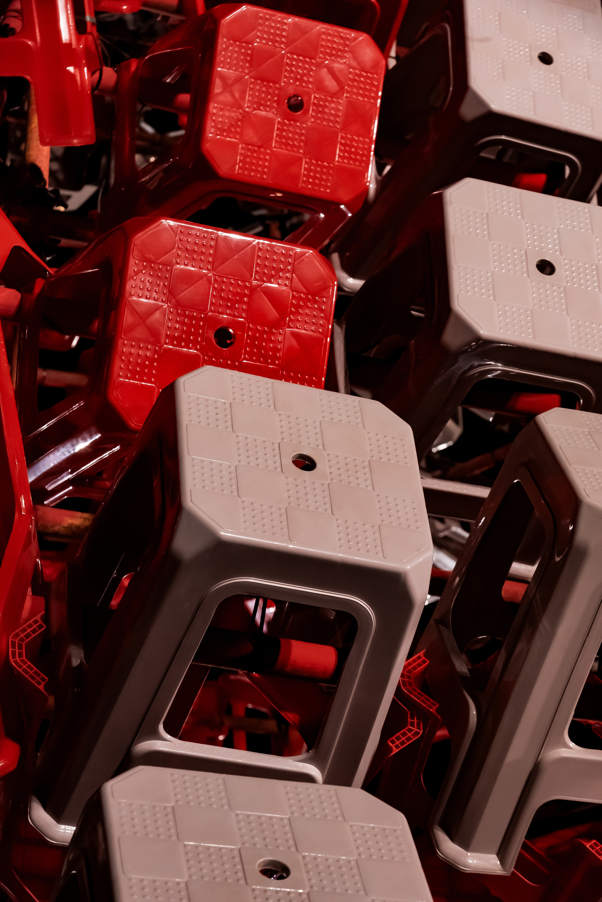 Detail of checkered stool seats in red and grey, each with a central hole, packed tightly together under night lighting