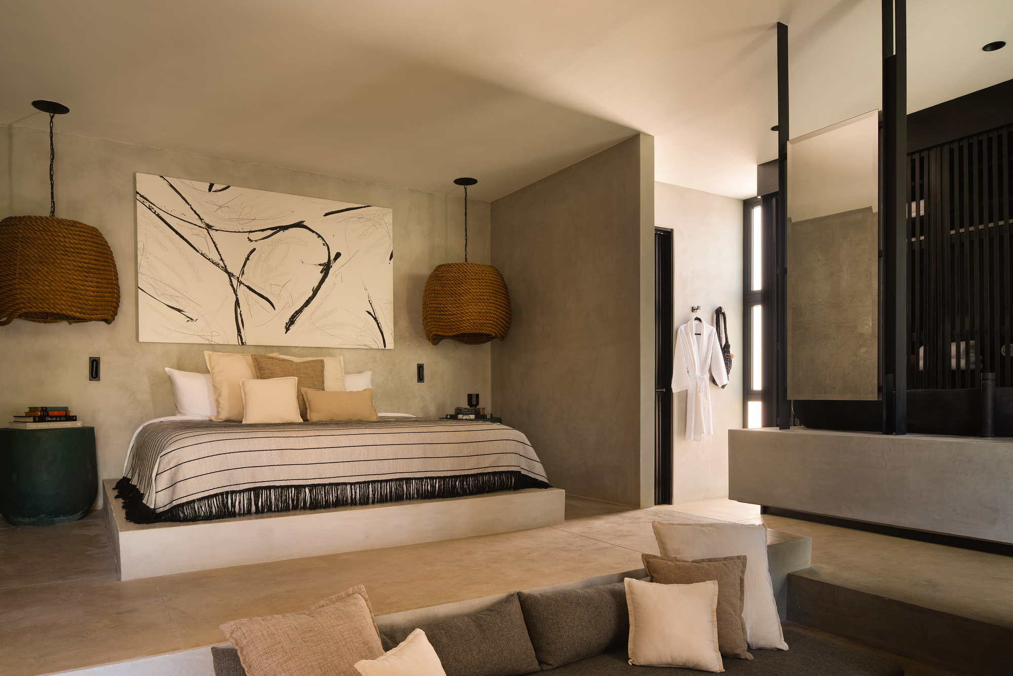 Bedroom with a raised plaster platform bed, rope pendant lamps and a brushstroke painting, a sunken seating area in the foreground