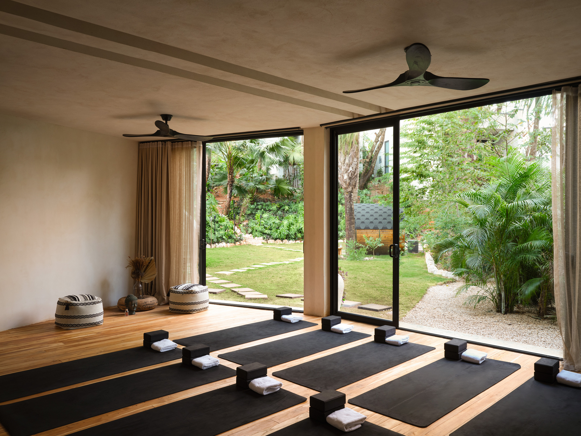 Yoga studio with black mats and folded towels facing sliding glass doors that open onto a lawn and palms