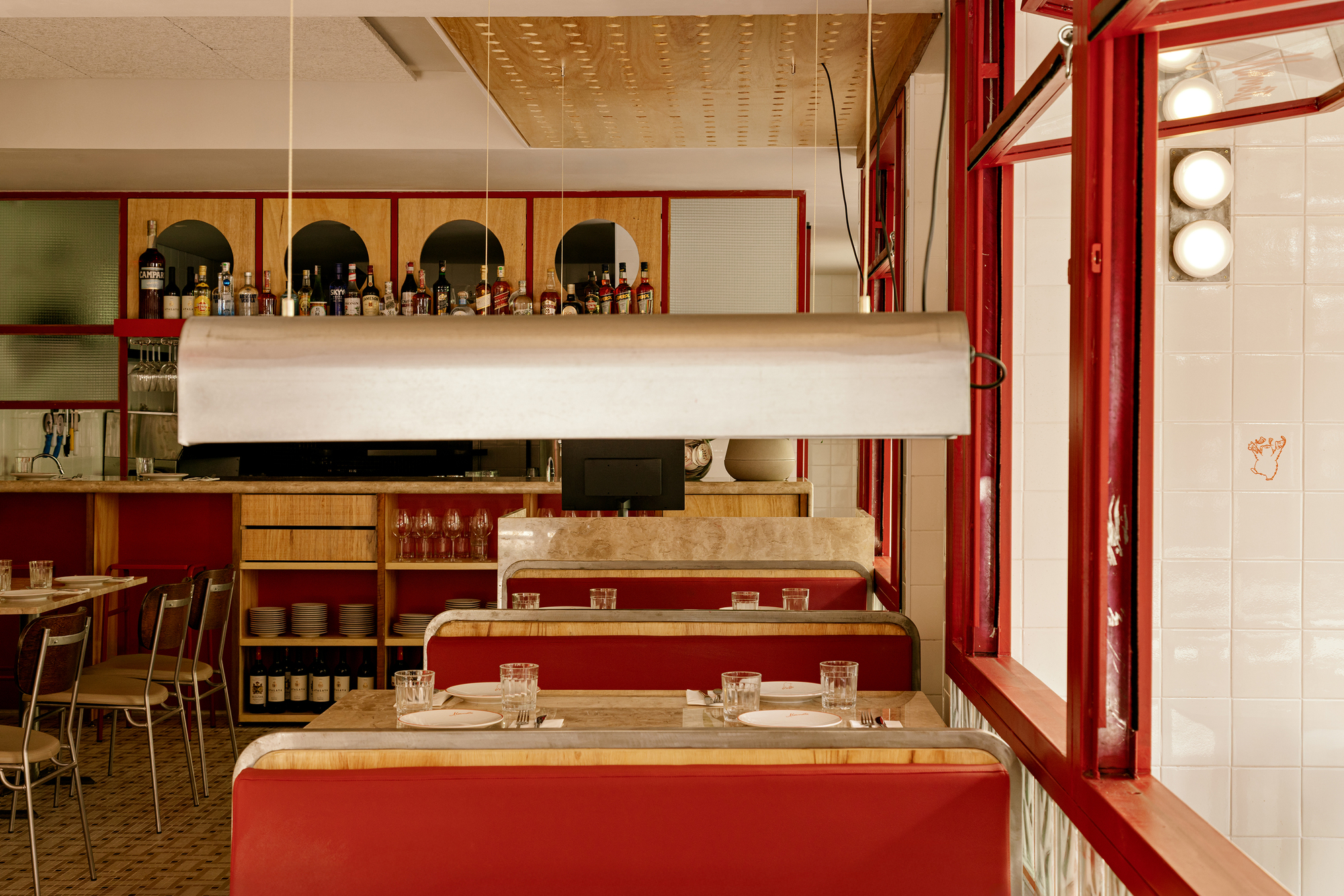 Red booths and a steel pendant lamp in front of the back bar, with a tiled window wall at right