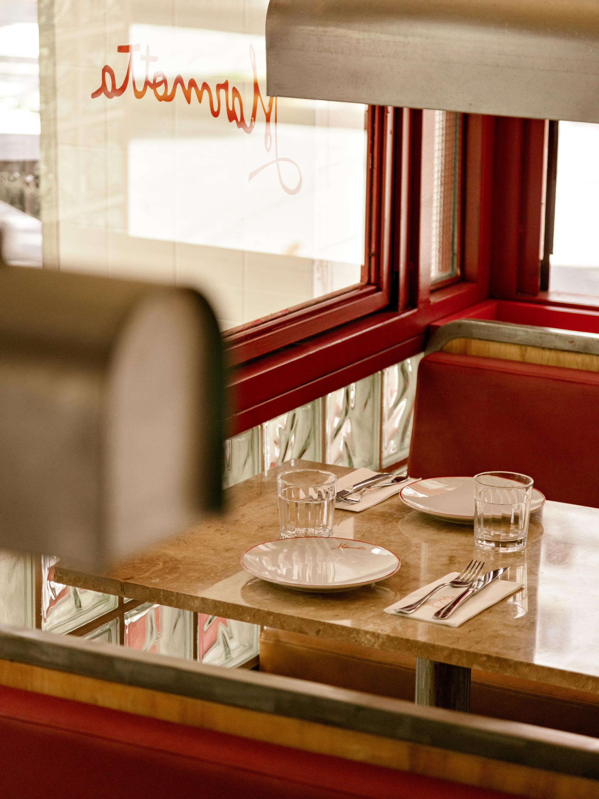 Marble-topped table set with plates and cutlery between red booth seats, a blurred steel pendant lamp in the foreground