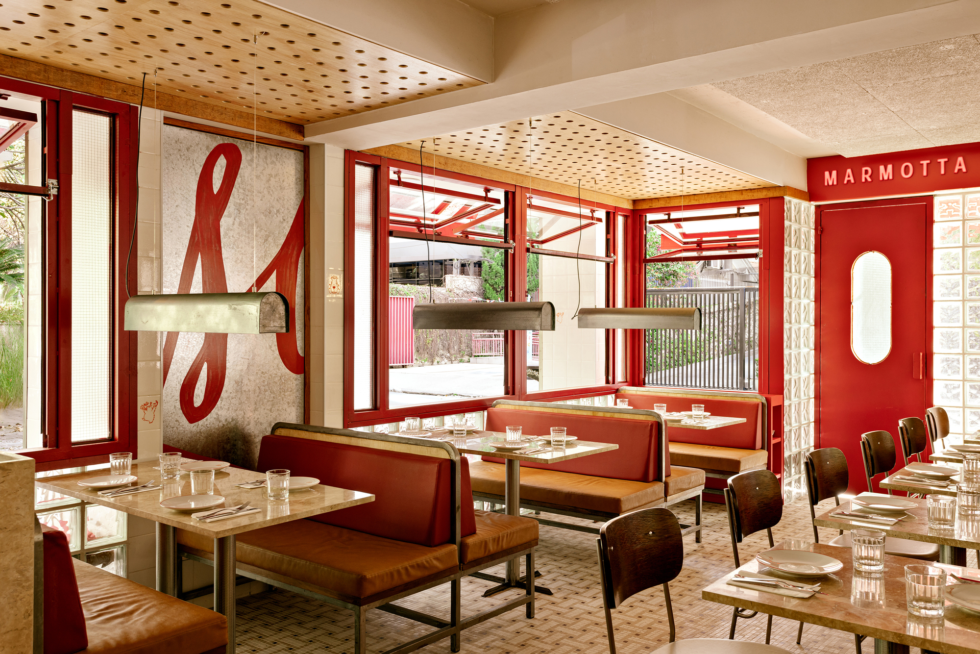 Wide dining room view with red booths, perforated timber ceiling, steel pendants and a large painted script letter on the wall