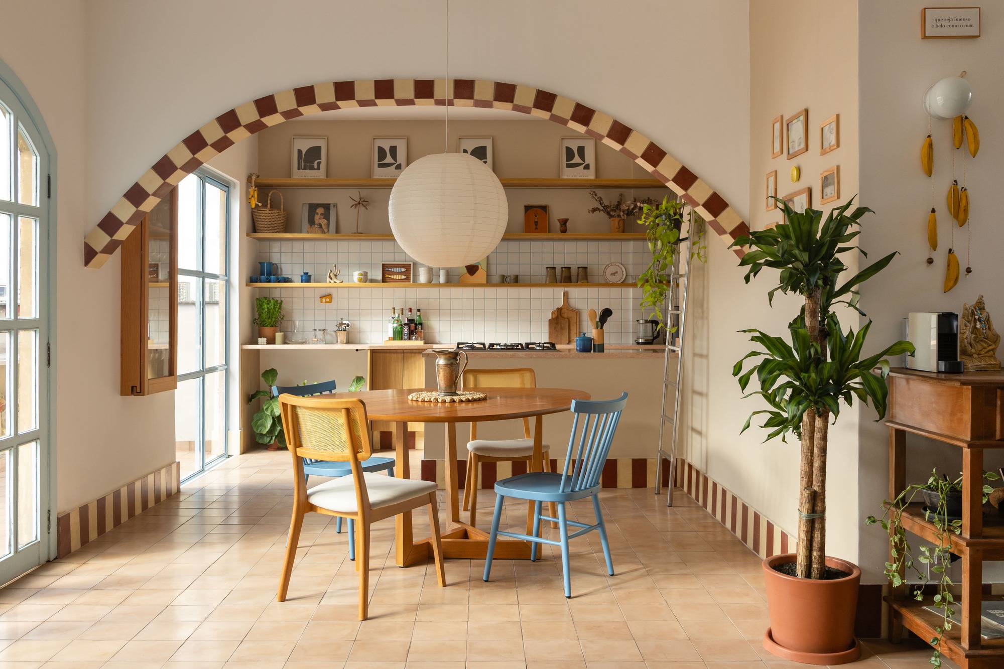 Dining area framed by an arch with a brown and cream checkered border, round wood table and blue chairs in daylight