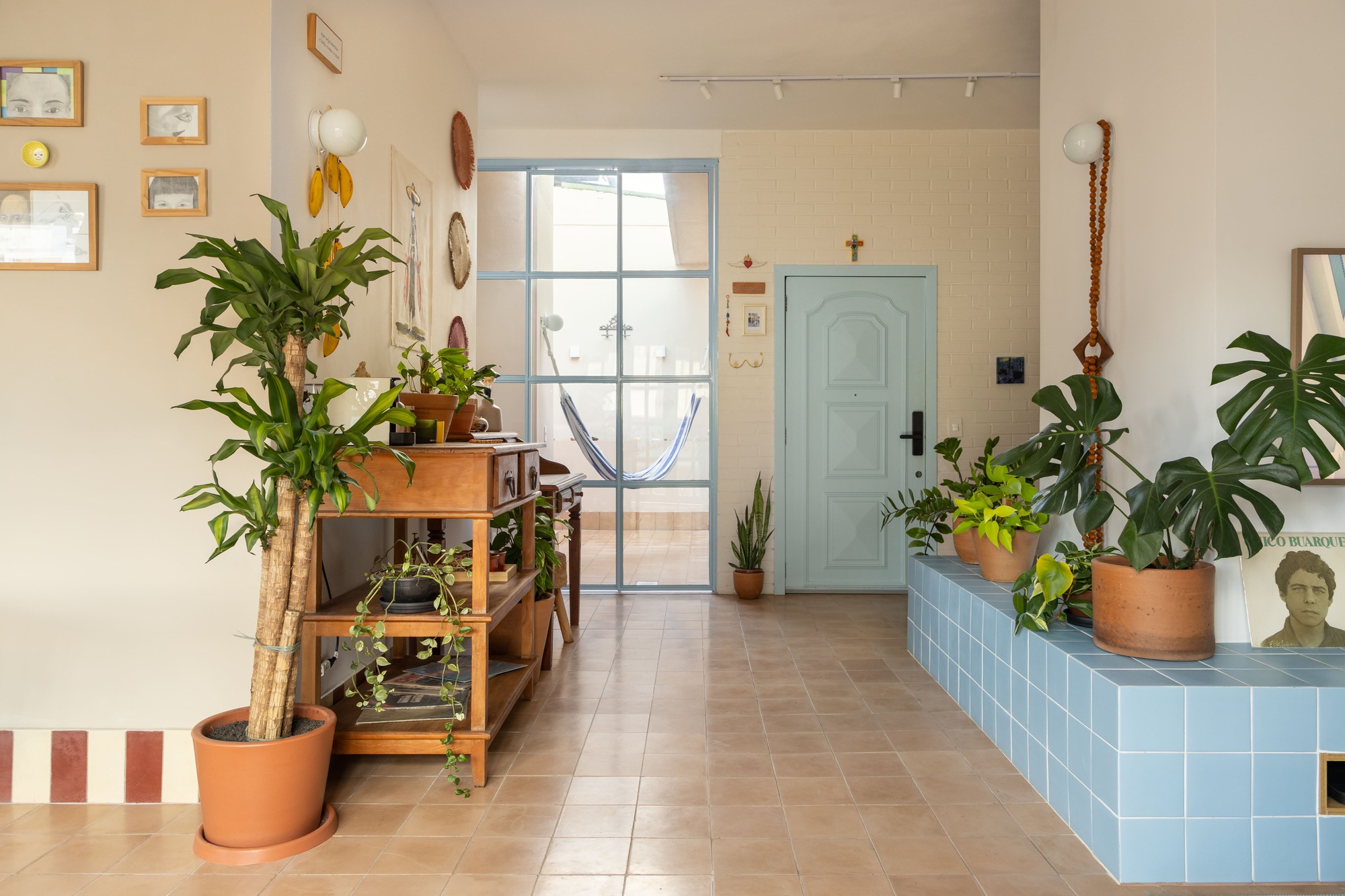 Entry hall with a pale blue door, steel-framed glazing and a blue tiled planter bench lined with monstera plants