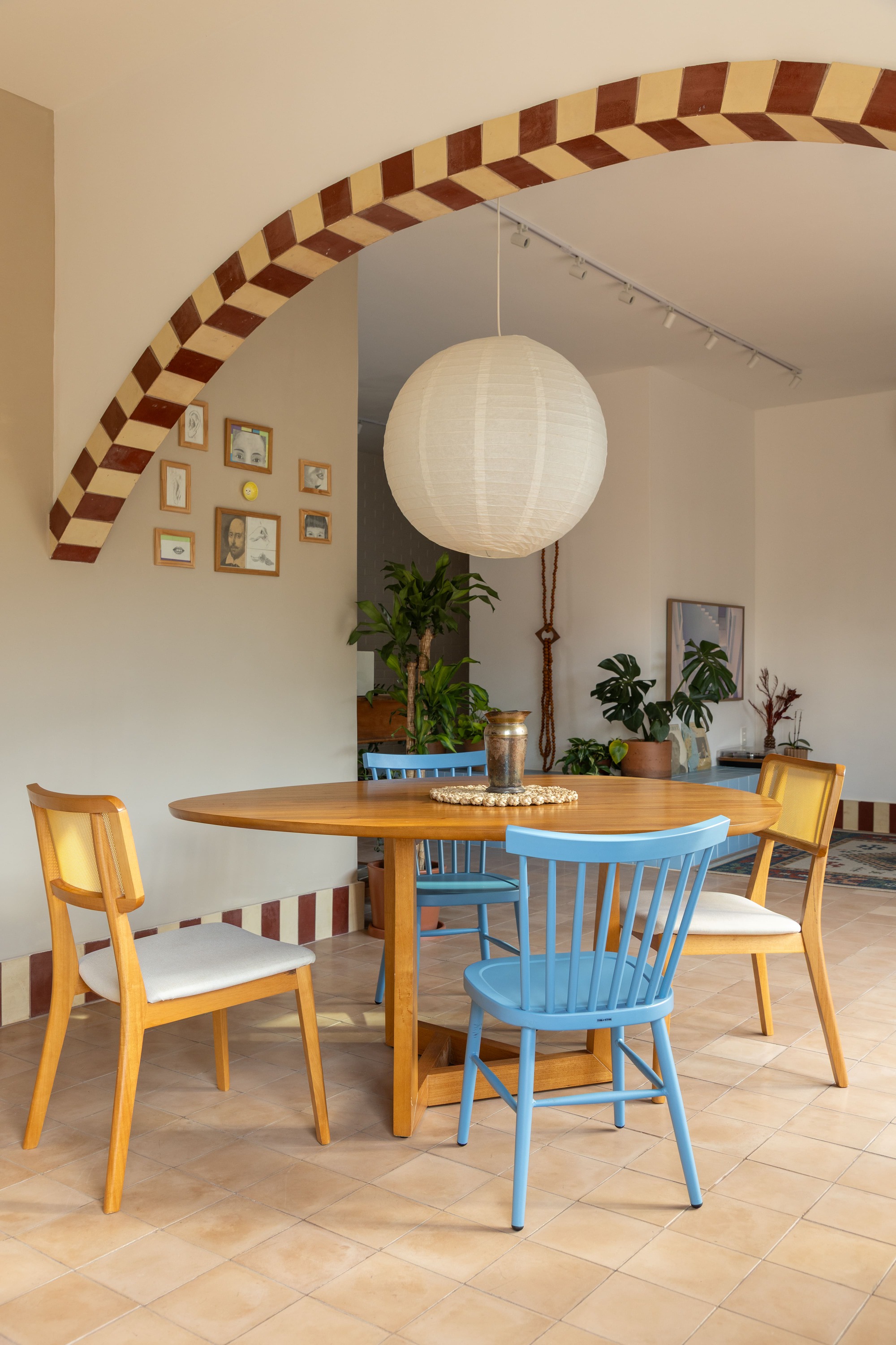 Round wood dining table with blue spindle chairs under a paper globe pendant and the checkered arch