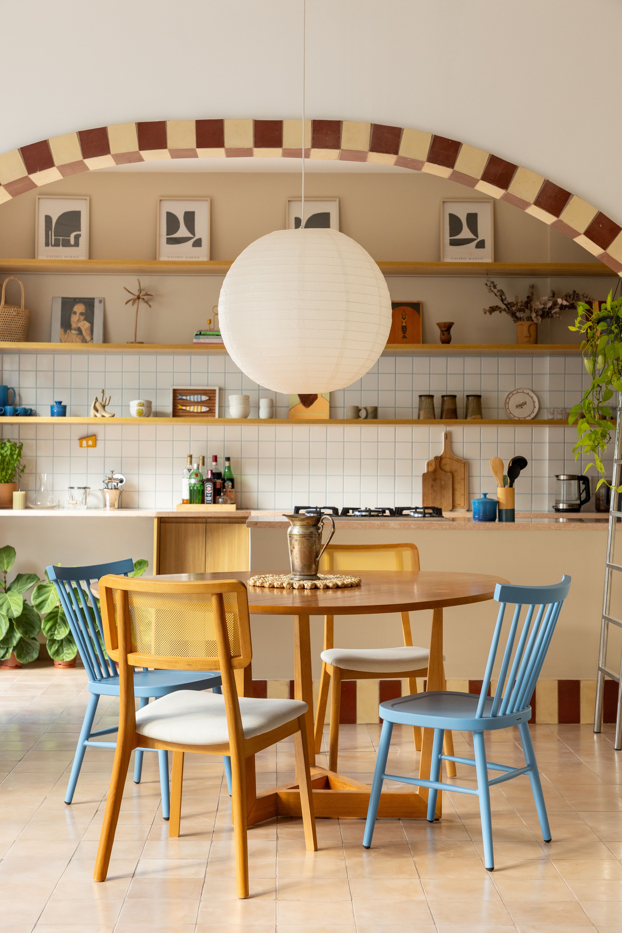 Round dining table with blue spindle chairs beneath a paper lantern and a checkered tile arch in soft daylight
