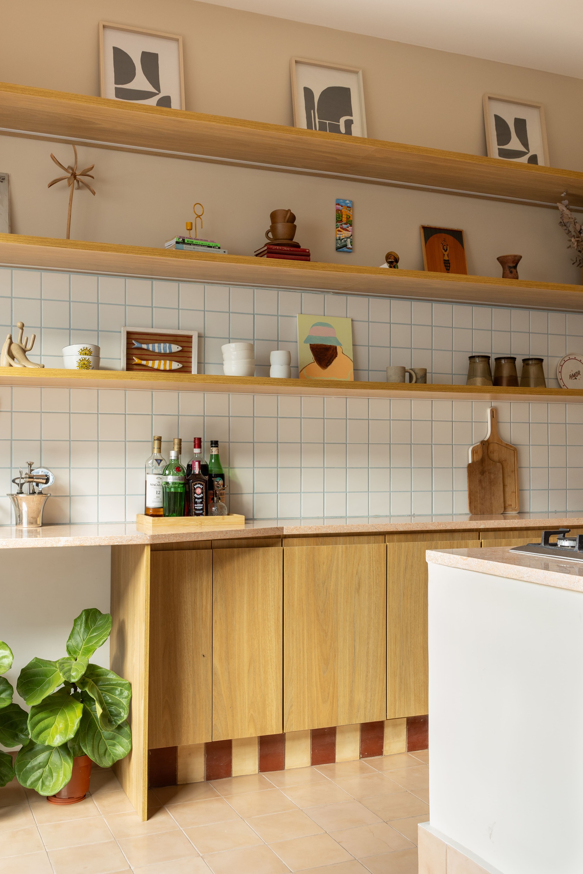 Kitchen wall with oak open shelves, white square tile backsplash and oak cabinets above a striped tile base, with a leafy plant
