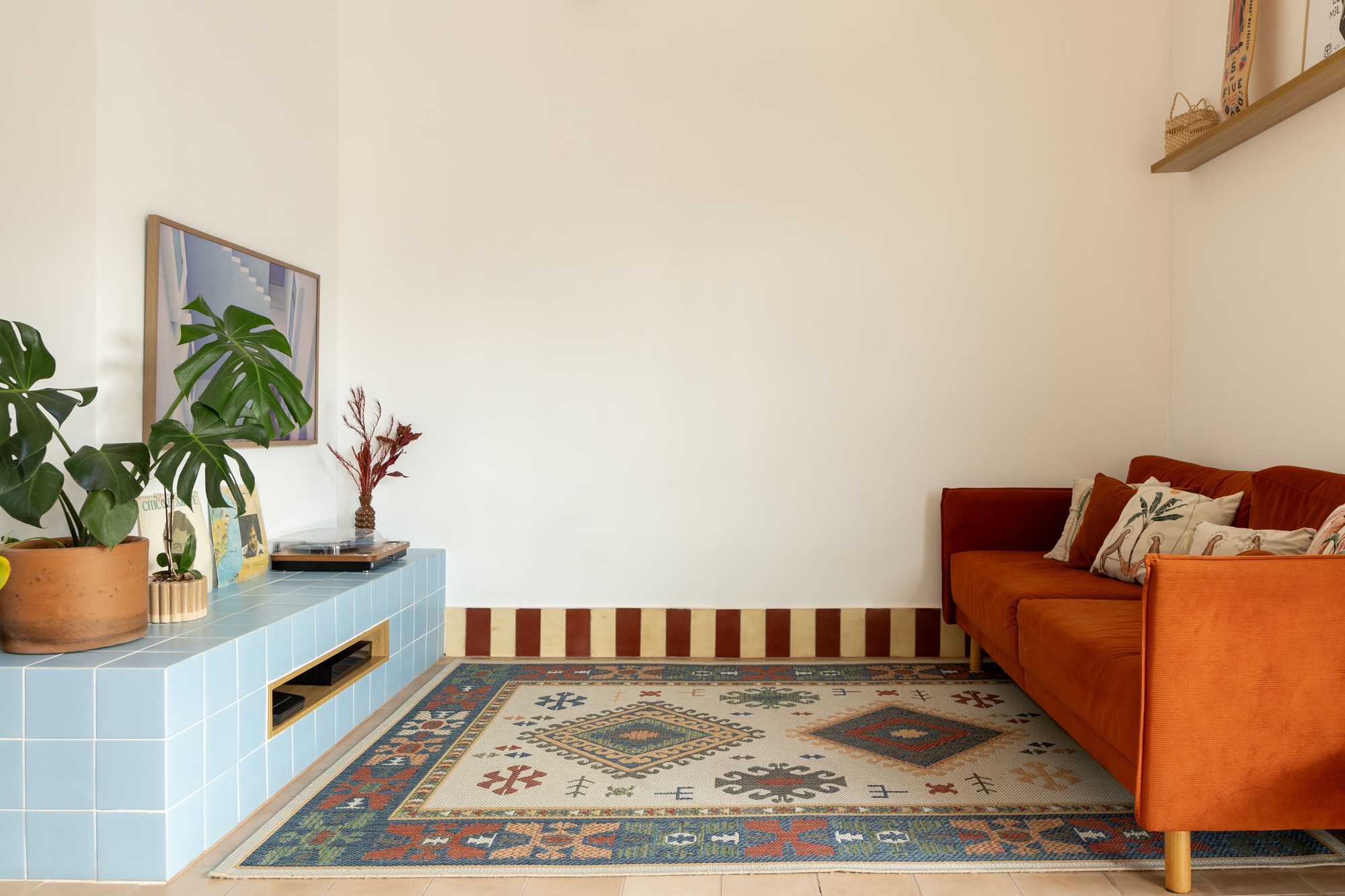 Orange velvet sofa on a patterned rug beside the blue tiled platform, with a red and cream striped wall band